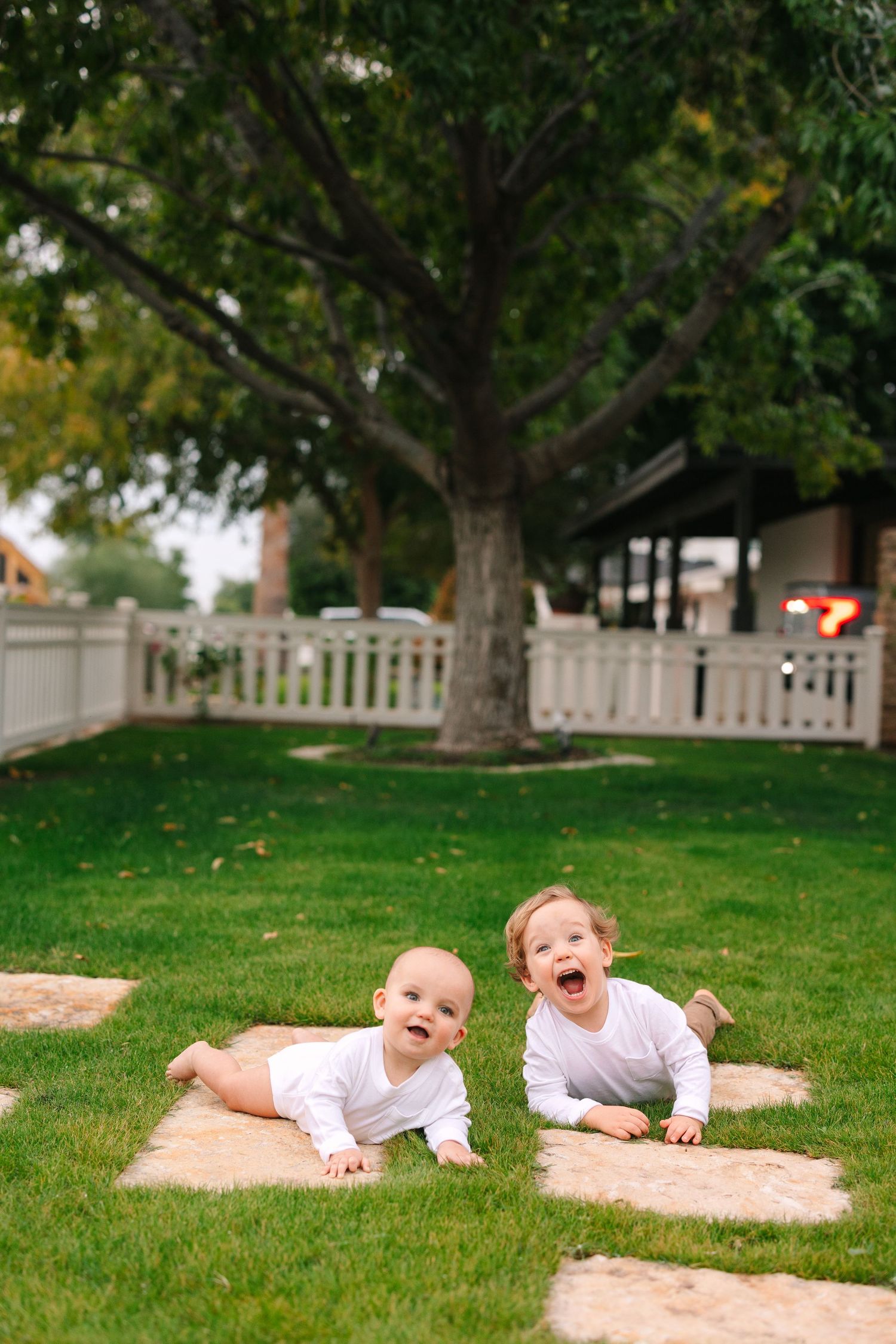 Children lying and laughing on soft blankets spread across green grass in a backyard setting.