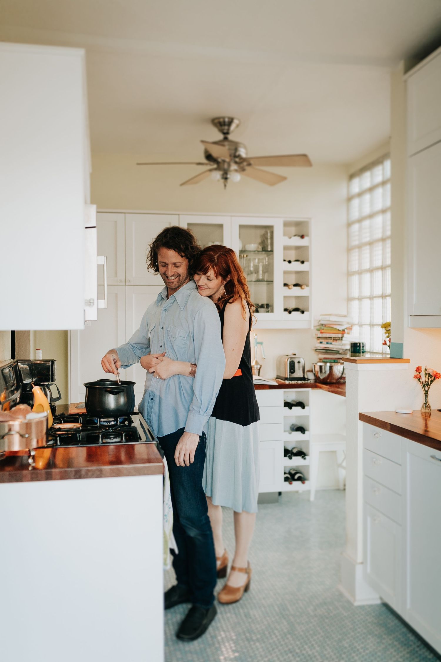 Couple dancing together in bright modern kitchen with white cabinets and hardwood floors.