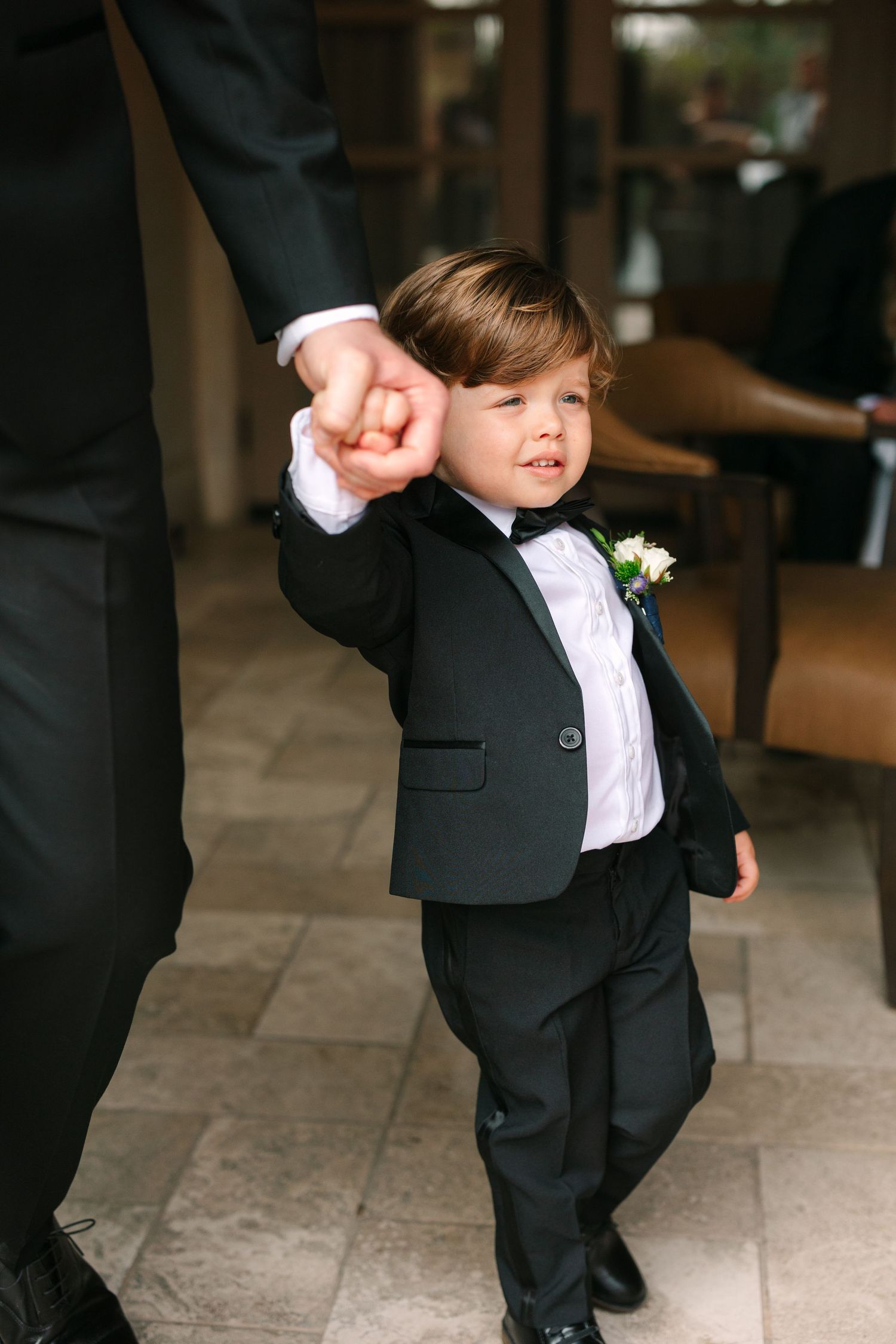 Young ring bearer in formal suit dances at indoor wedding venue.