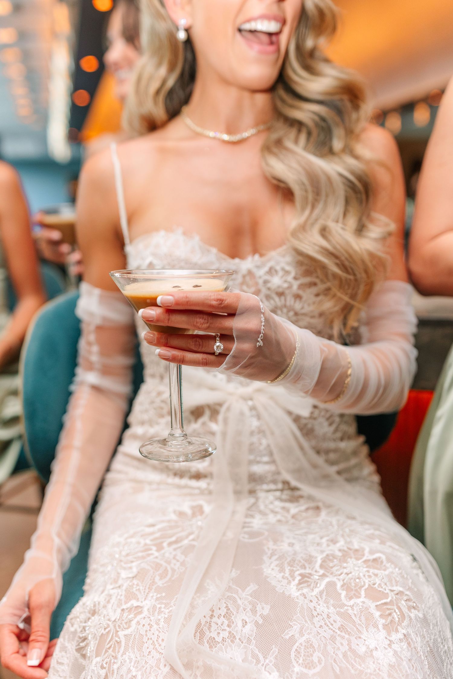 Bride in lace dress holding champagne cocktail during wedding reception.