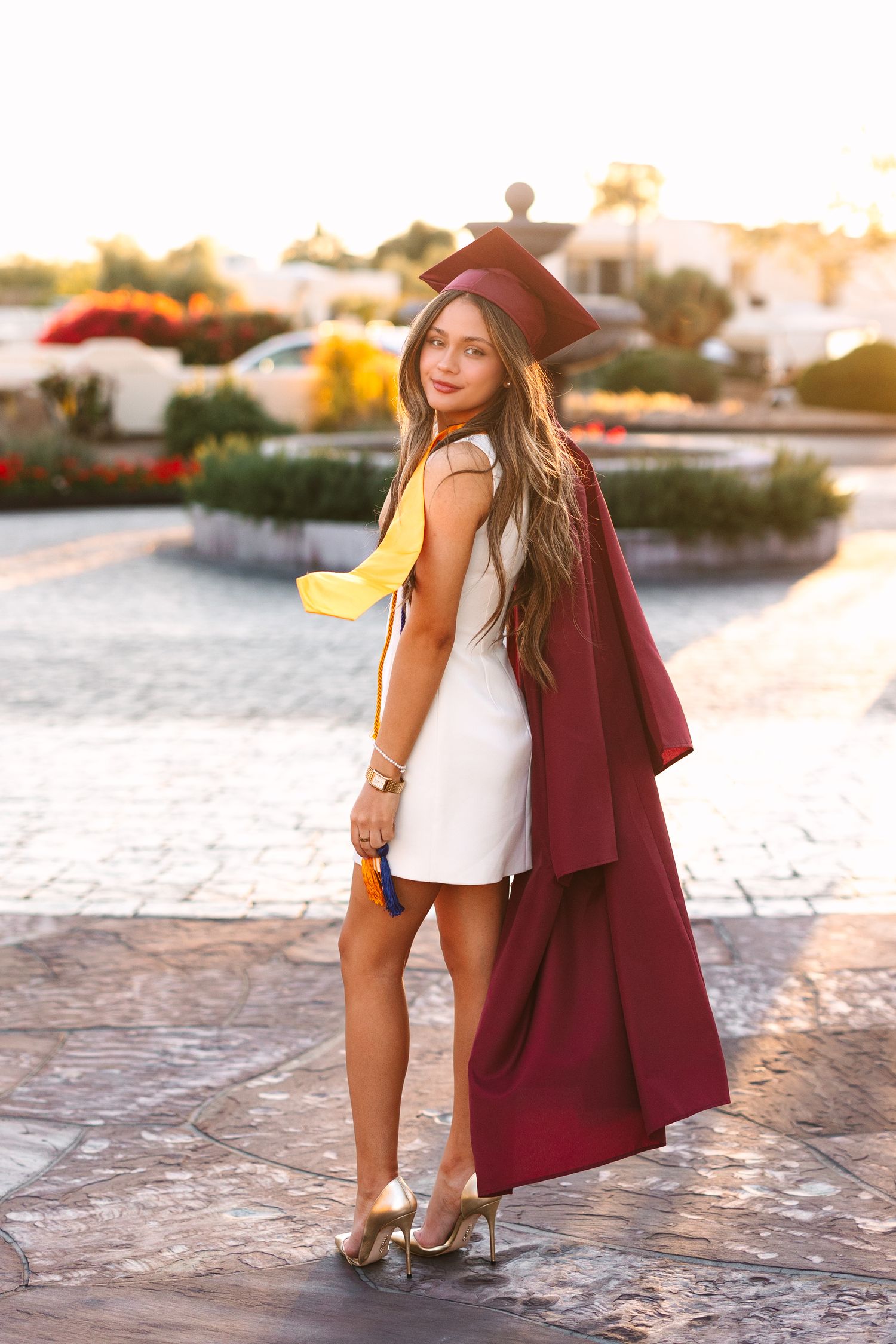 A fashionable autumn outfit featuring a burgundy blazer, white top and floppy hat photographed at sunset on cobblestone streets.