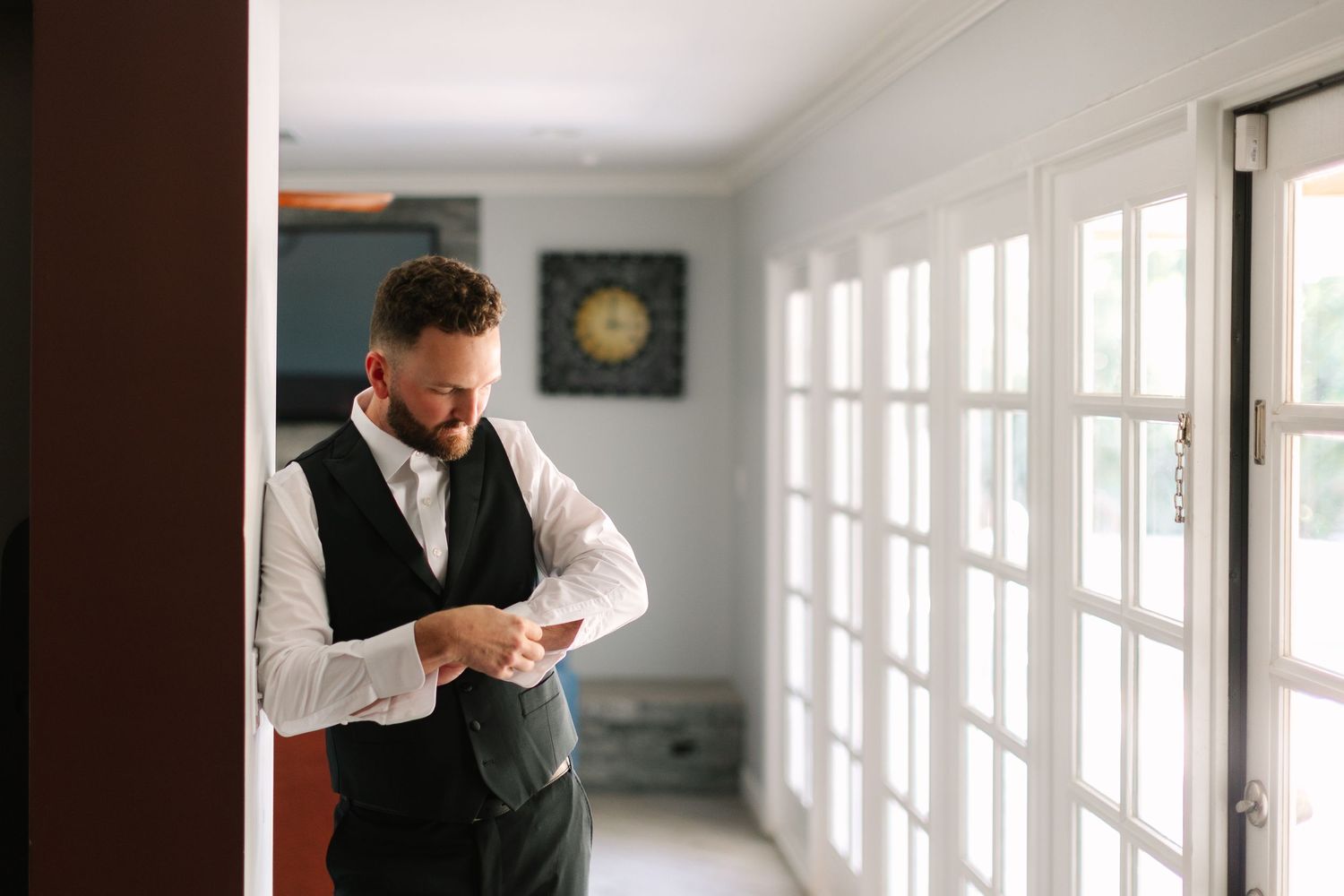 Getting ready moment in bright hallway with French doors and natural light.