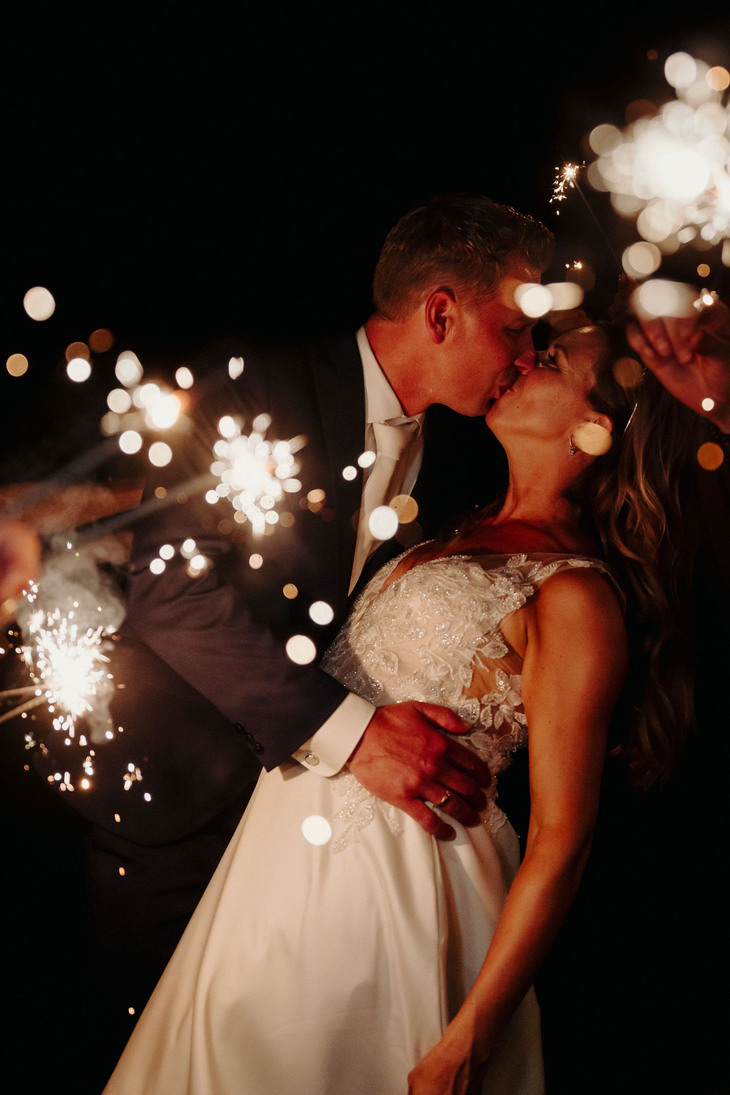 A romantic nighttime wedding photo with sparklers creating magical bokeh effects.