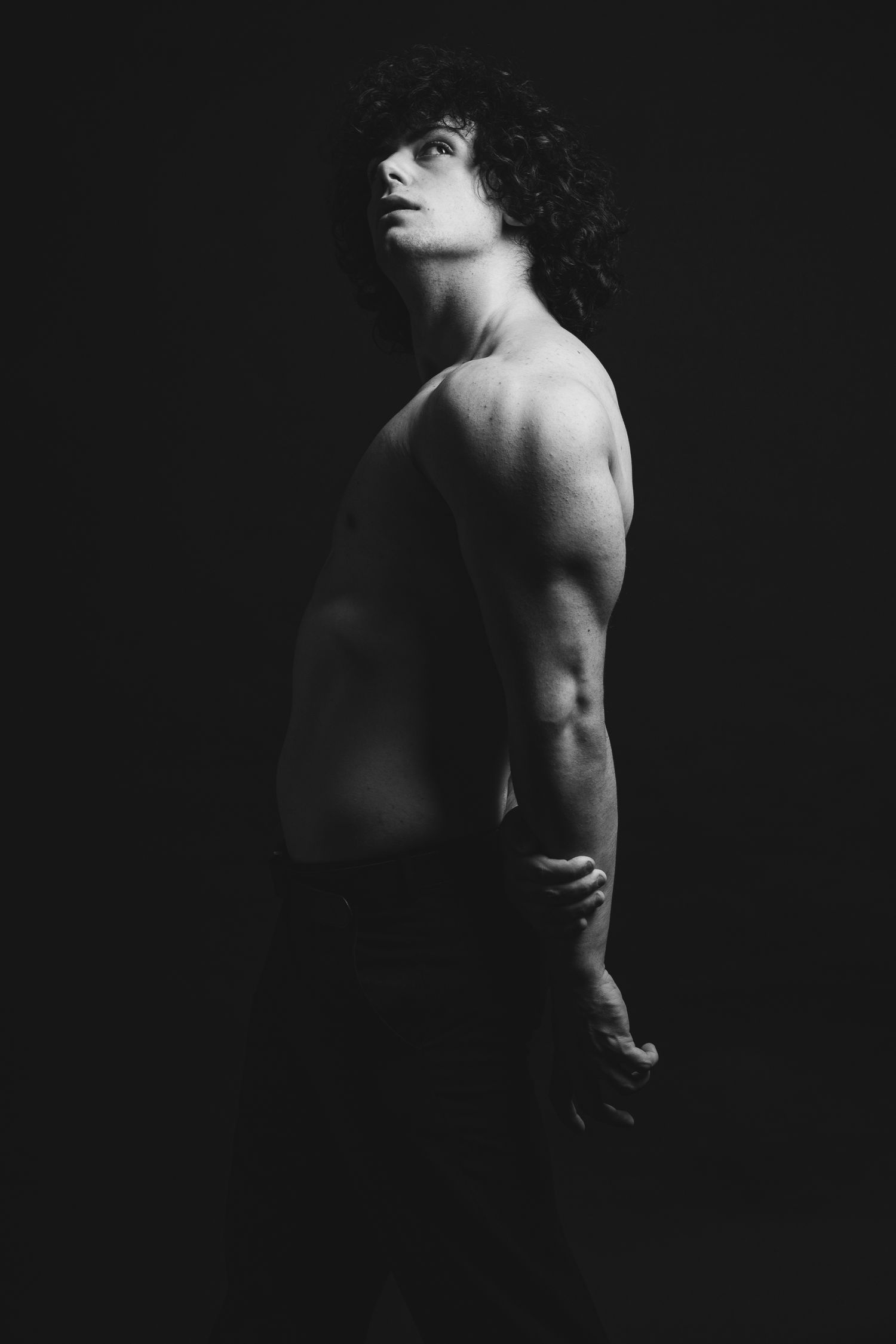 Artistic black and white portrait showing muscular physique against dark background.