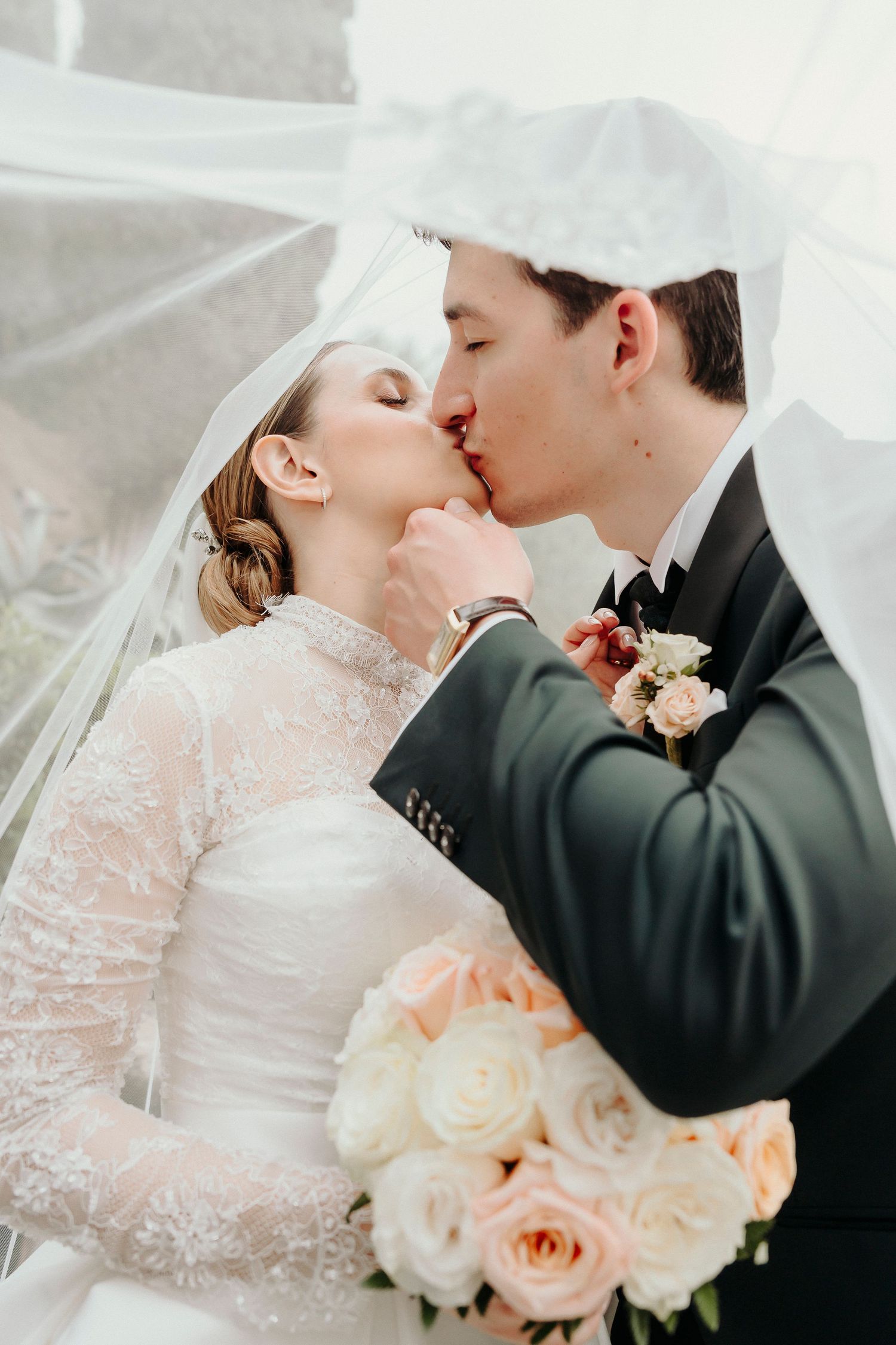 An elegant wedding portrait with delicate lace veil and peach rose bouquet.