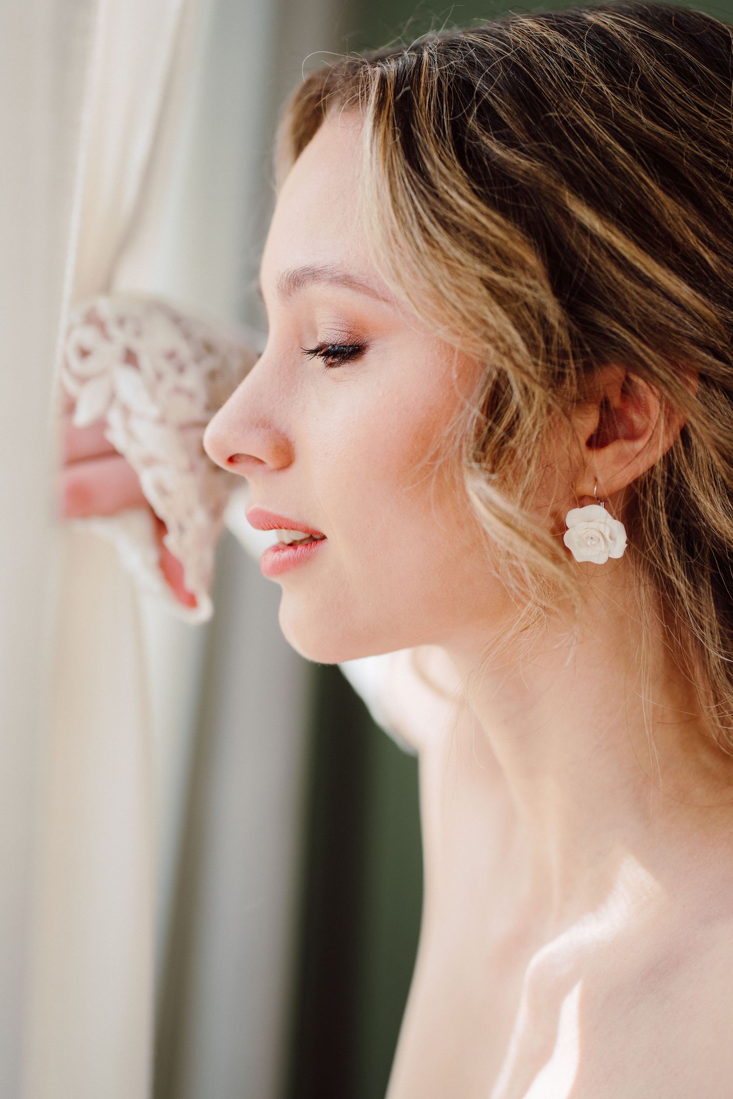 Close-up portrait showcasing delicate bridal jewelry and soft makeup in natural light.
