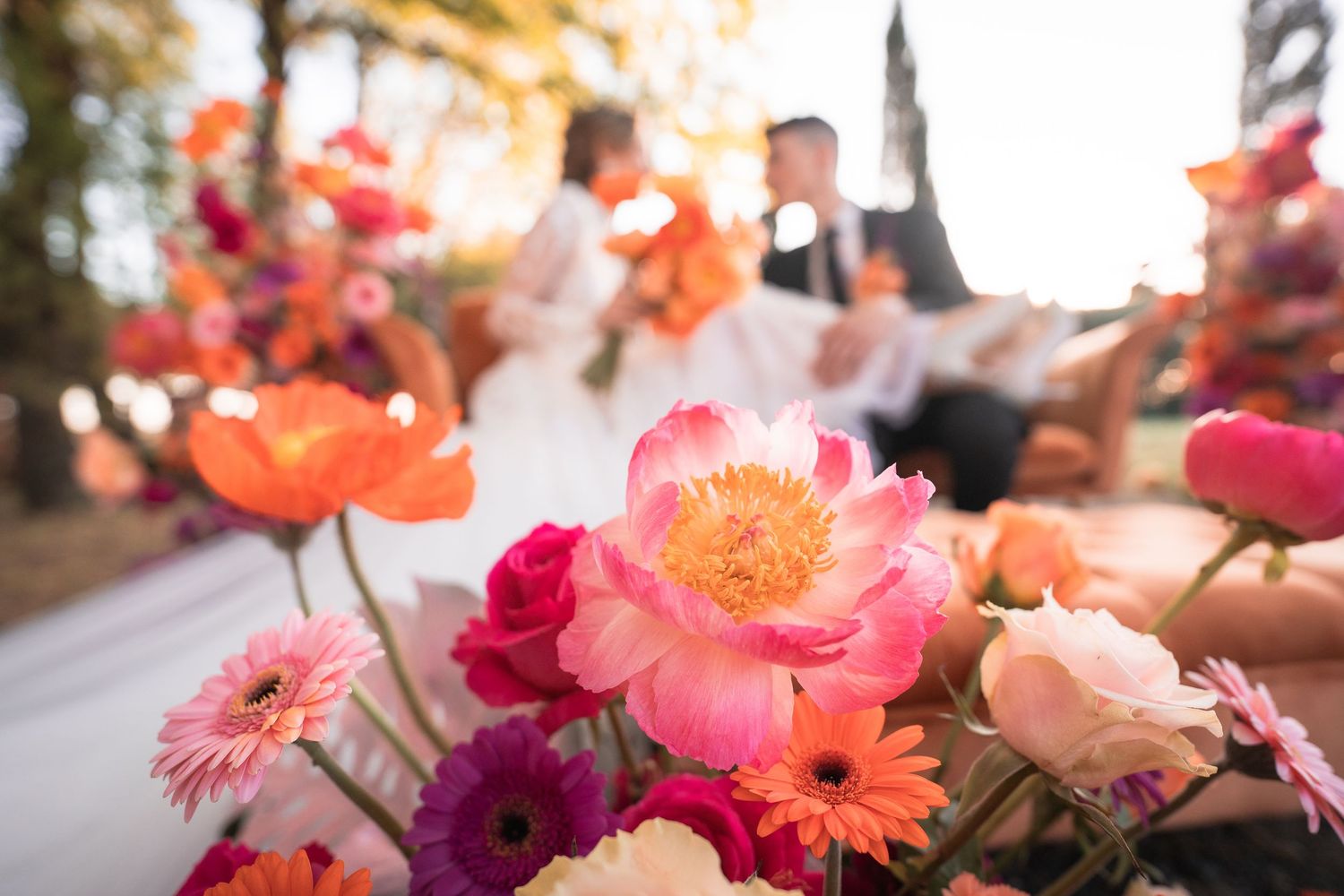 A unique wedding moment with the couple sitting on a vintage floral sofa, surrounded by nature and decorative flowers.