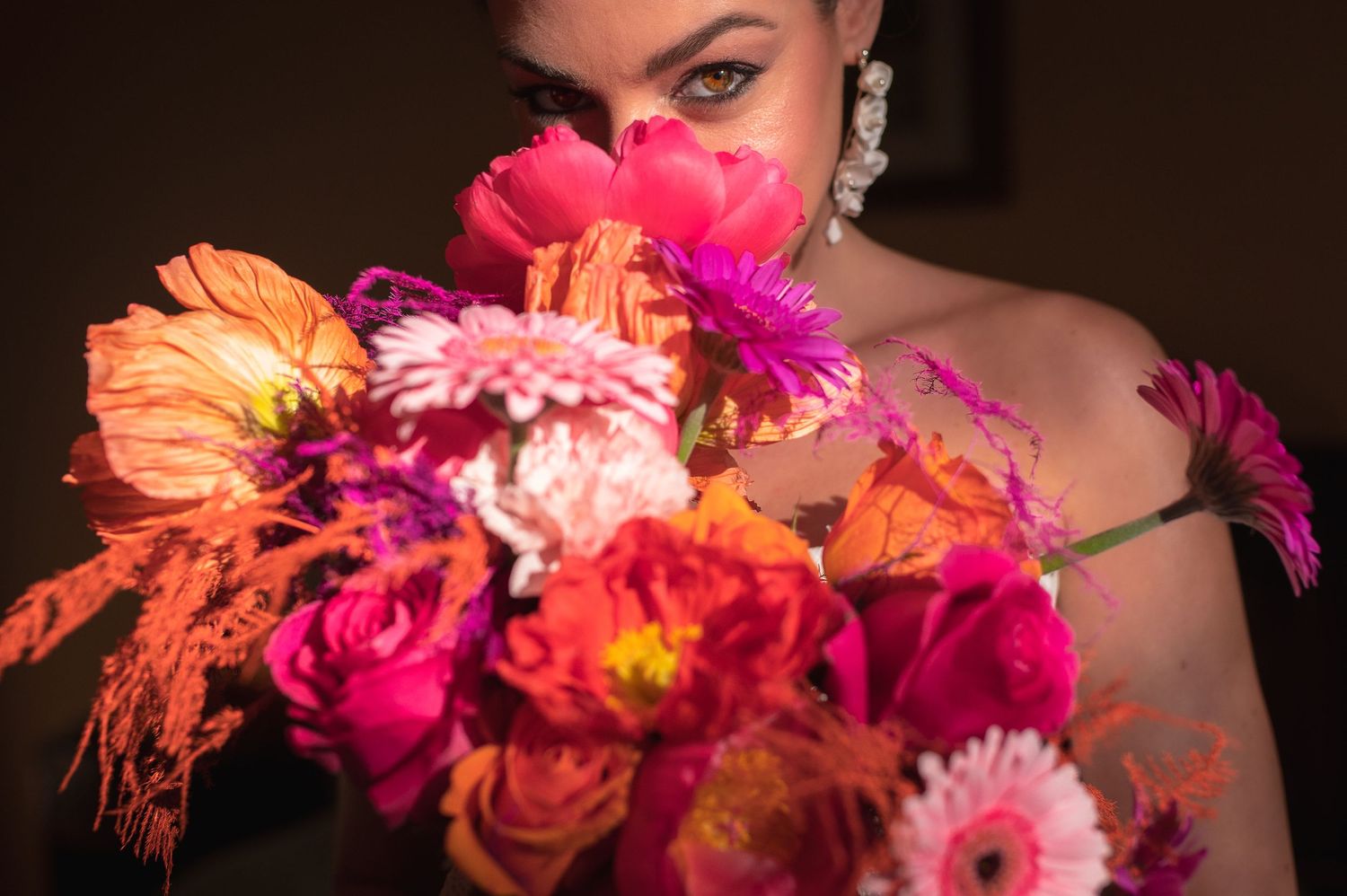 Dramatic close-up of vibrant orange and pink bridal bouquet with flowers in focus.