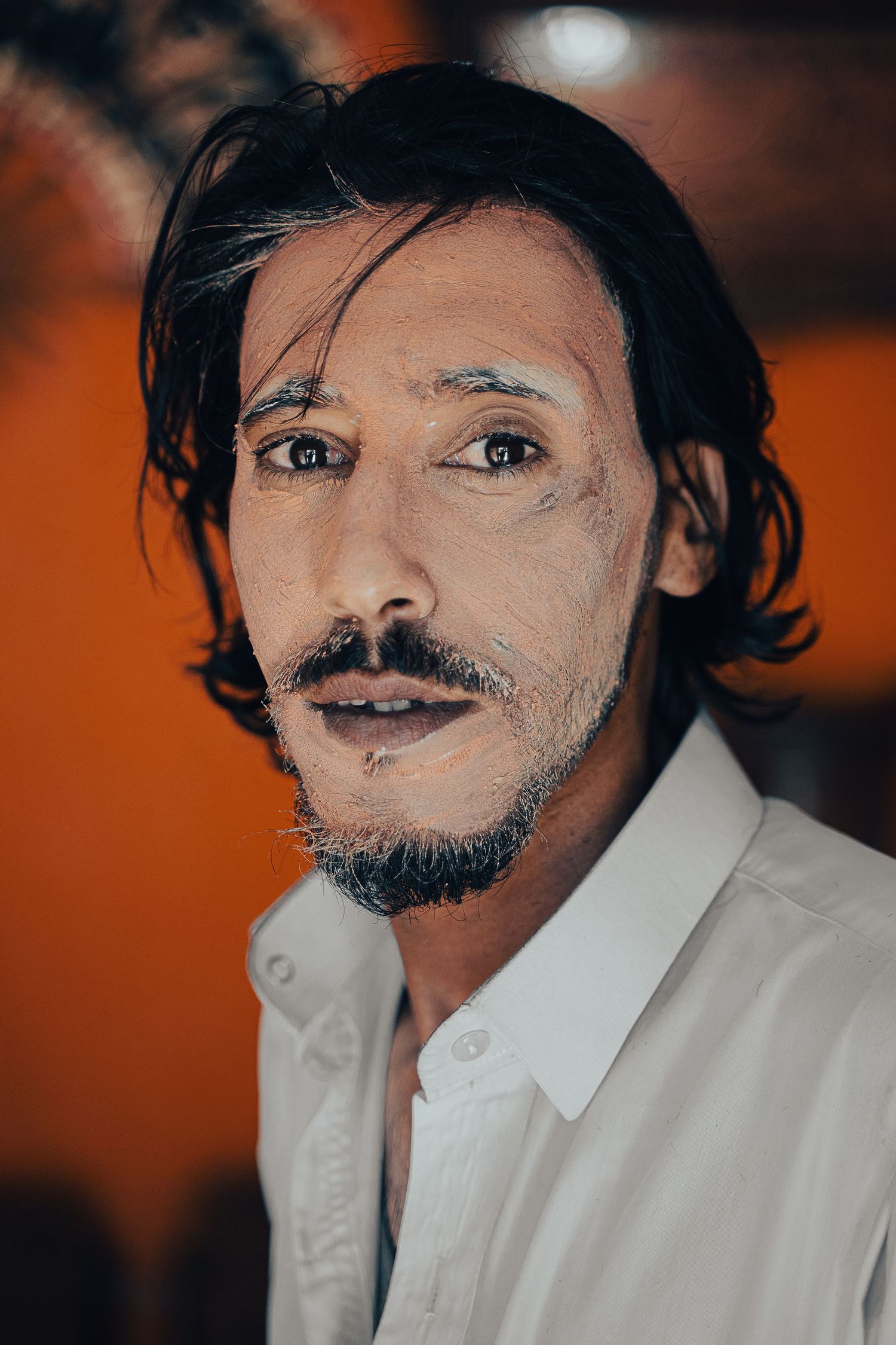 A dramatic portrait against an orange background showing dark hair and a white collar.