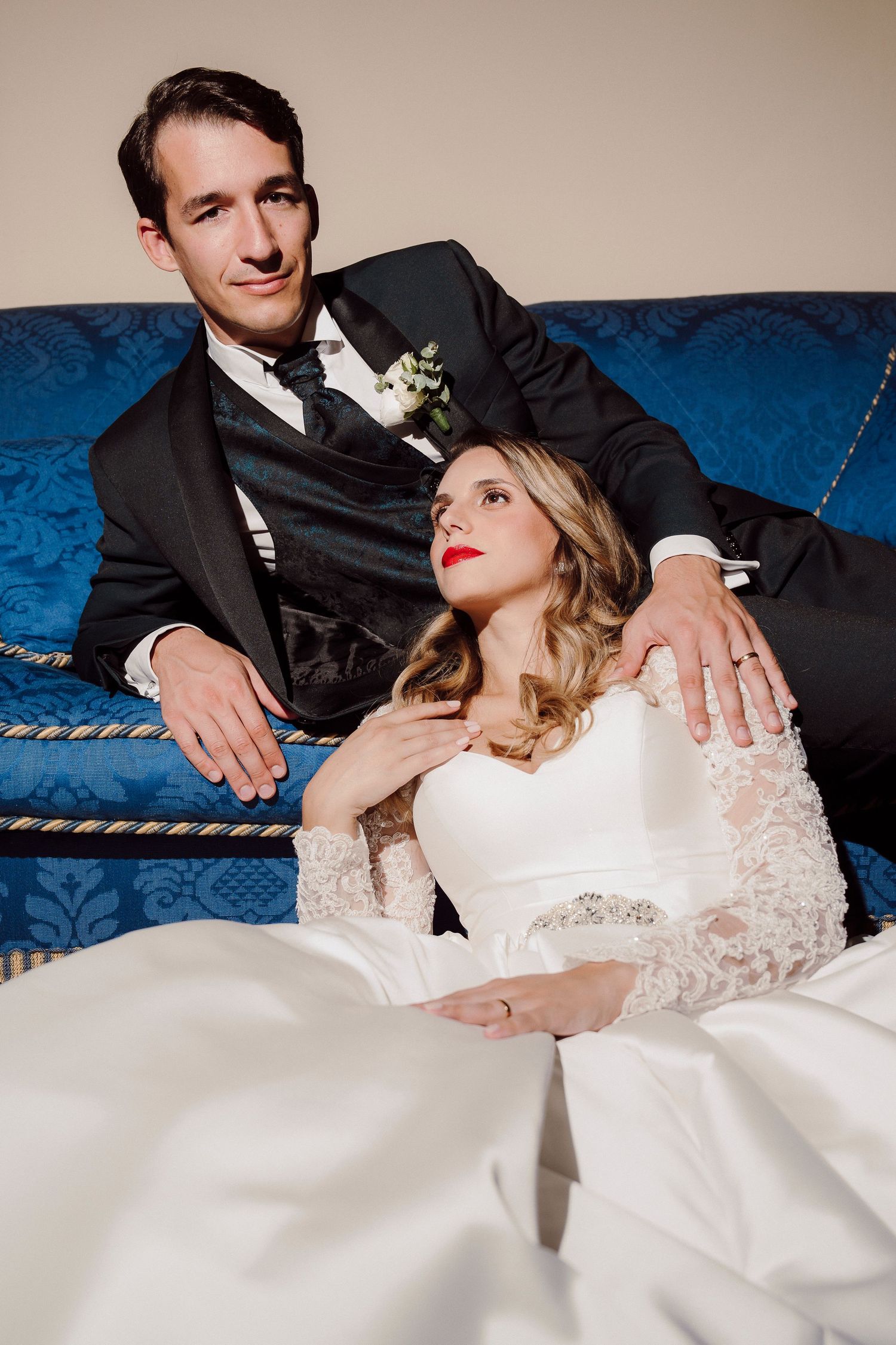 Glamorous wedding couple posing intimately on a blue velvet couch.