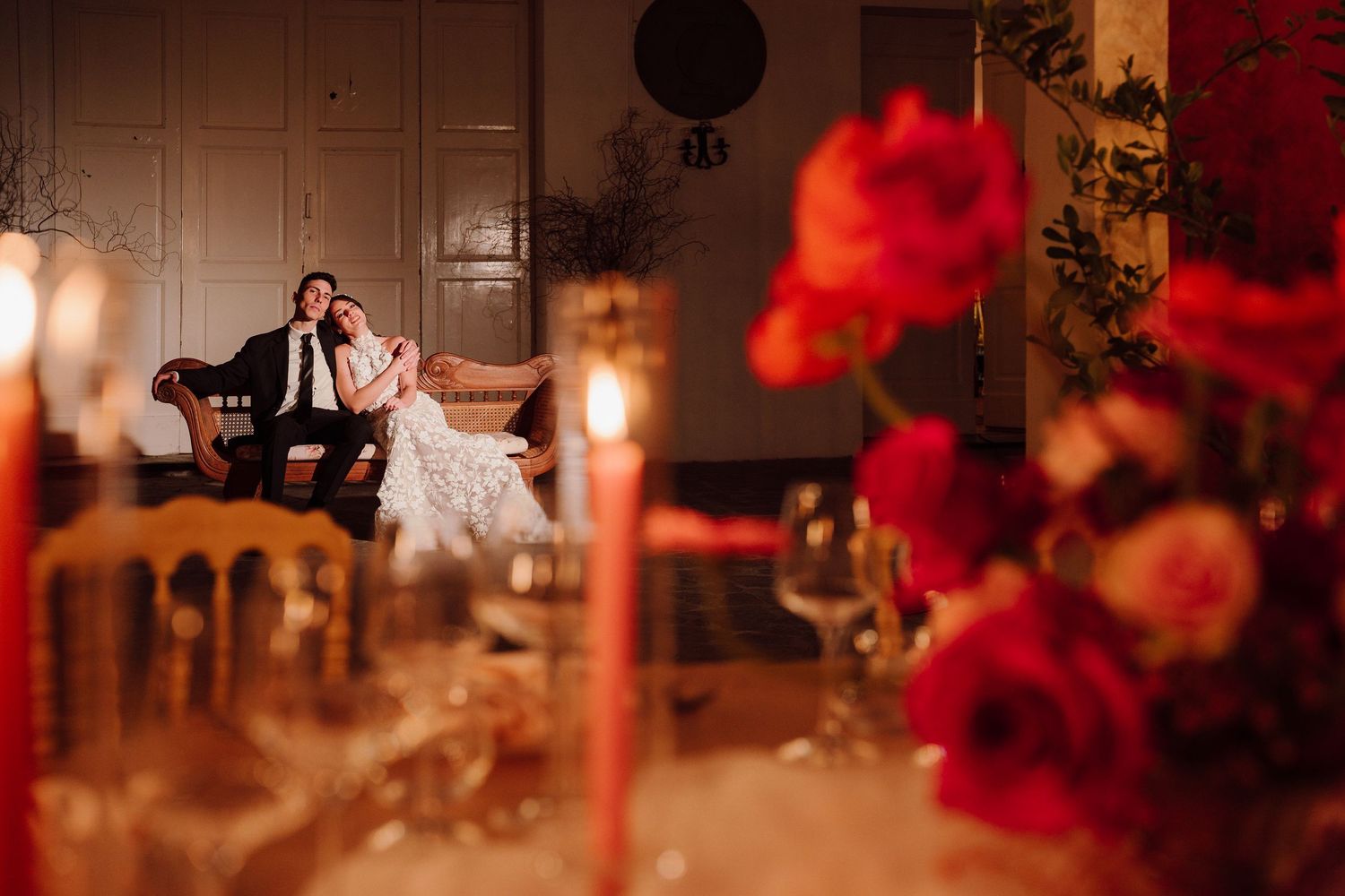 A unique wedding moment with the couple sitting on a vintage floral sofa, surrounded by nature and decorative flowers.
