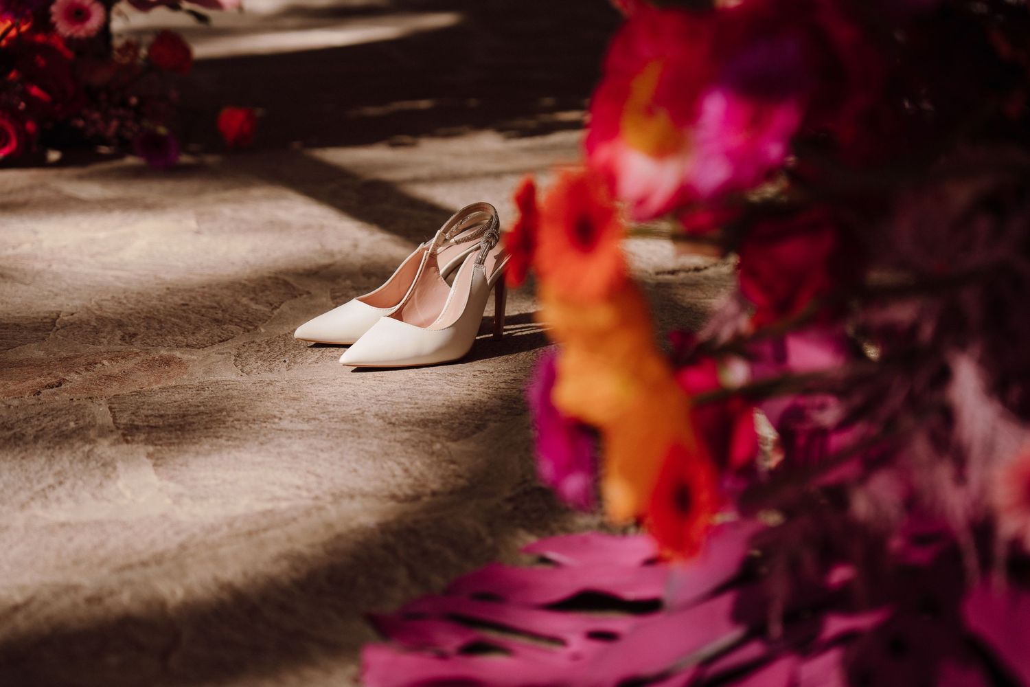 Elegant bridal shoes on wooden floor with colorful flowers in soft lighting.