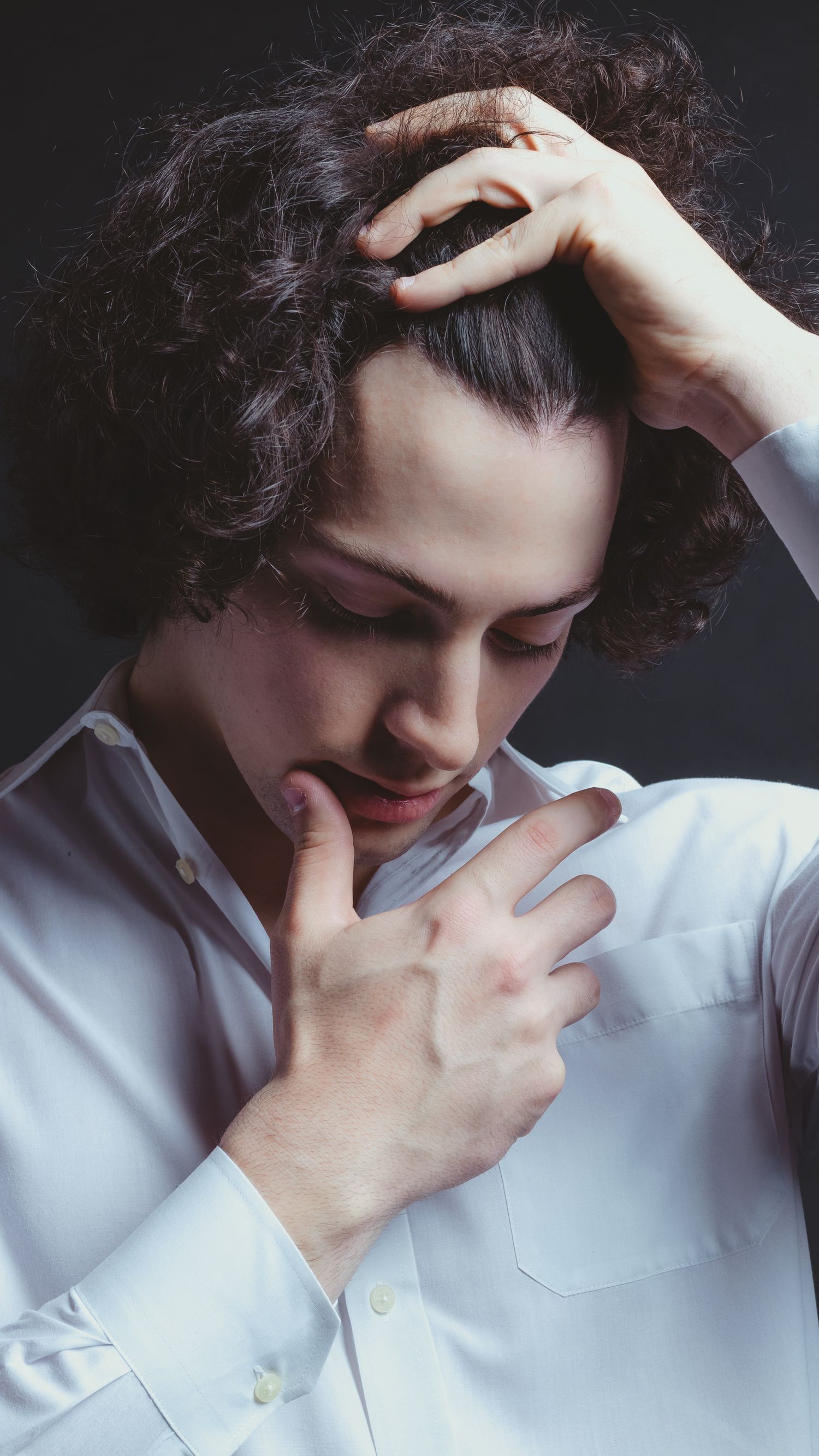 Portrait of someone in white shirt touching their curly hair thoughtfully.