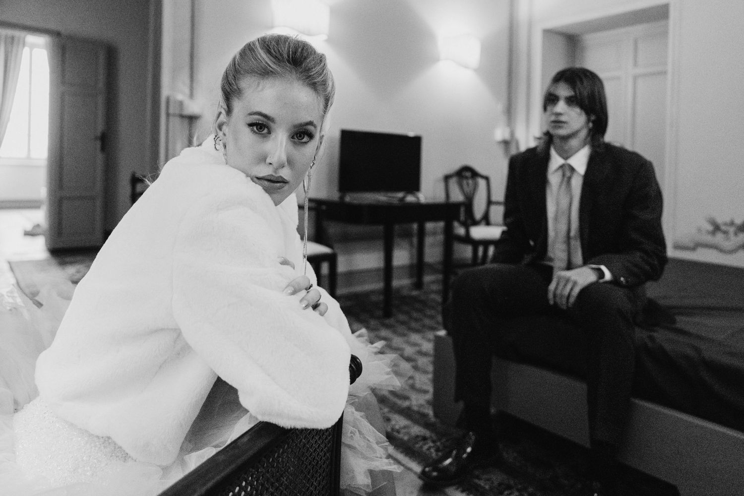 Elegant black and white wedding portrait in a hotel room with dramatic lighting.