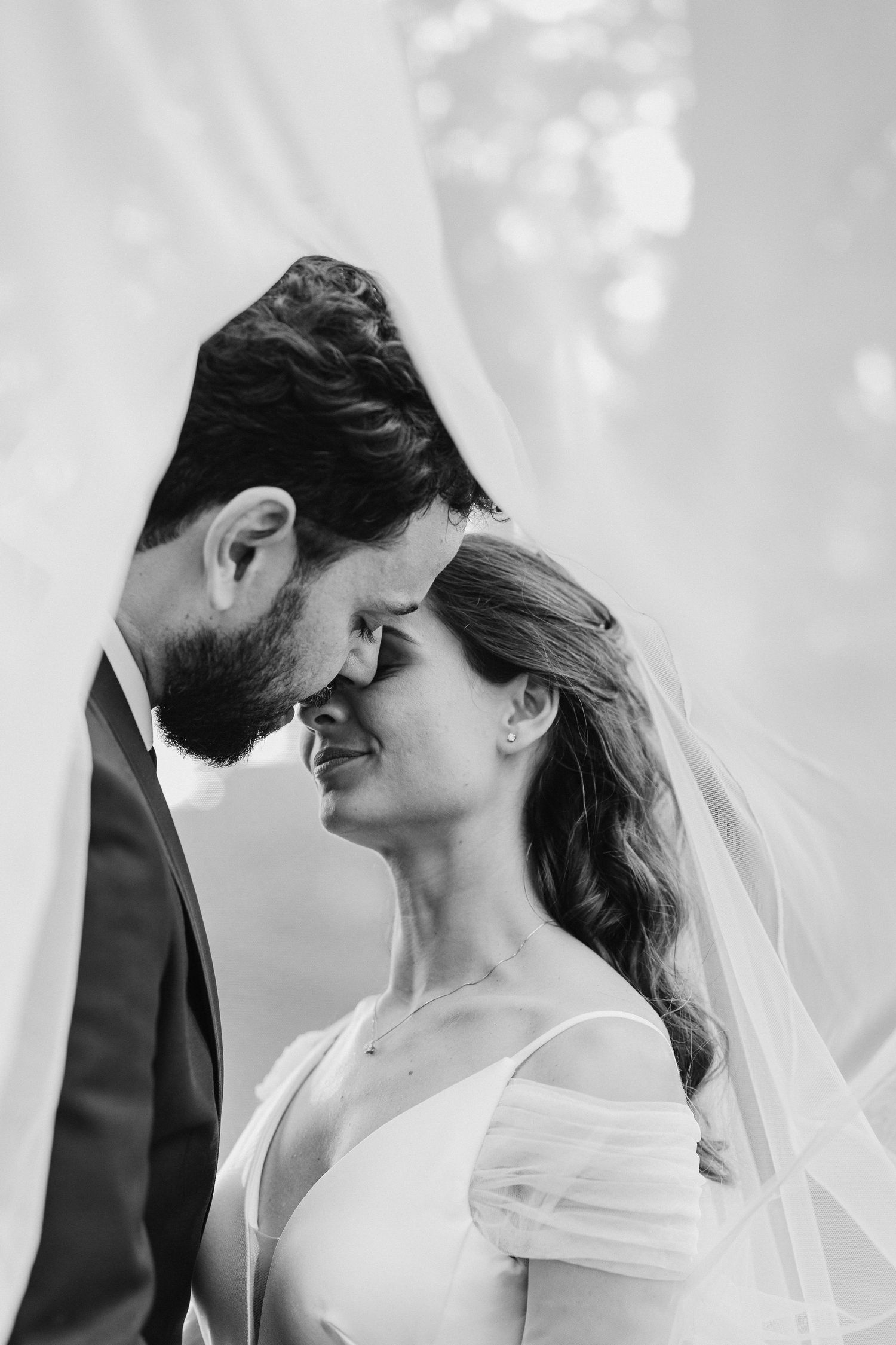 A romantic black and white wedding portrait of a couple sharing an intimate moment with flowing veil.