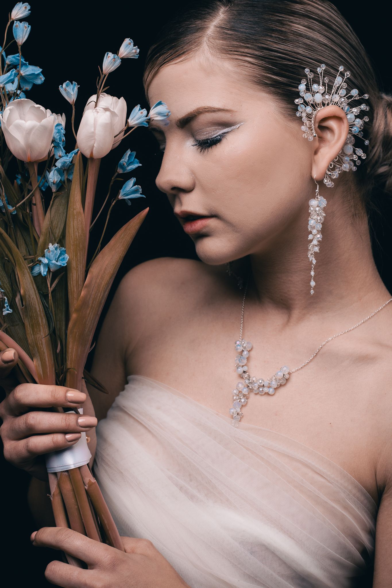 Elegant bridal portraits against dark background showcase ornate crystal jewelry with delicate white flowers as accents.