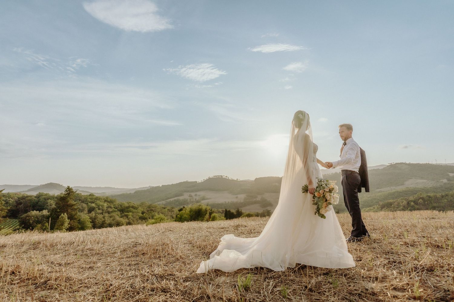 Wedding couple walking through a golden field with rolling hills in the background.