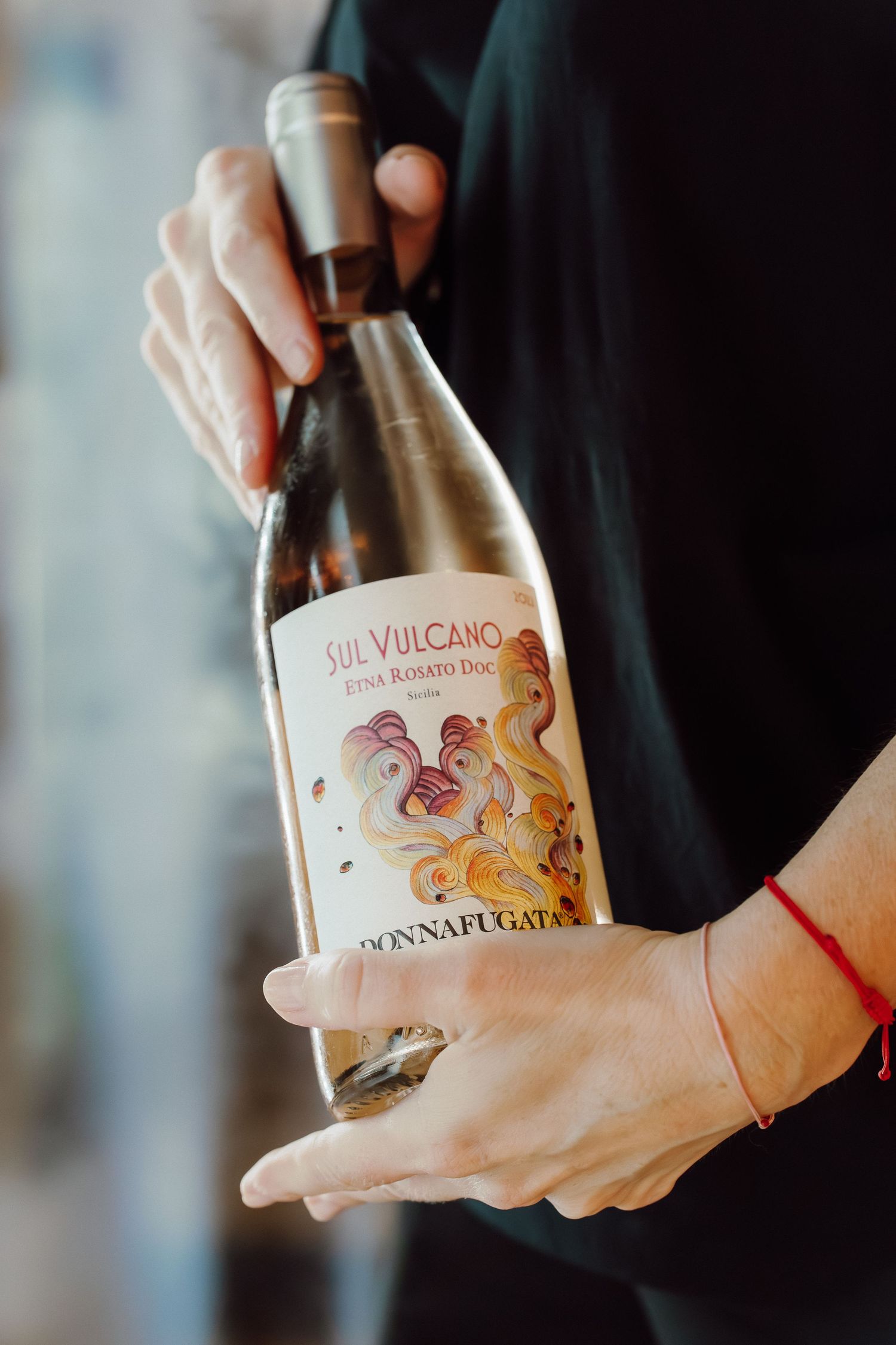 Hands holding a wine bottle labeled 'OH VULCANO' with artistic label design.