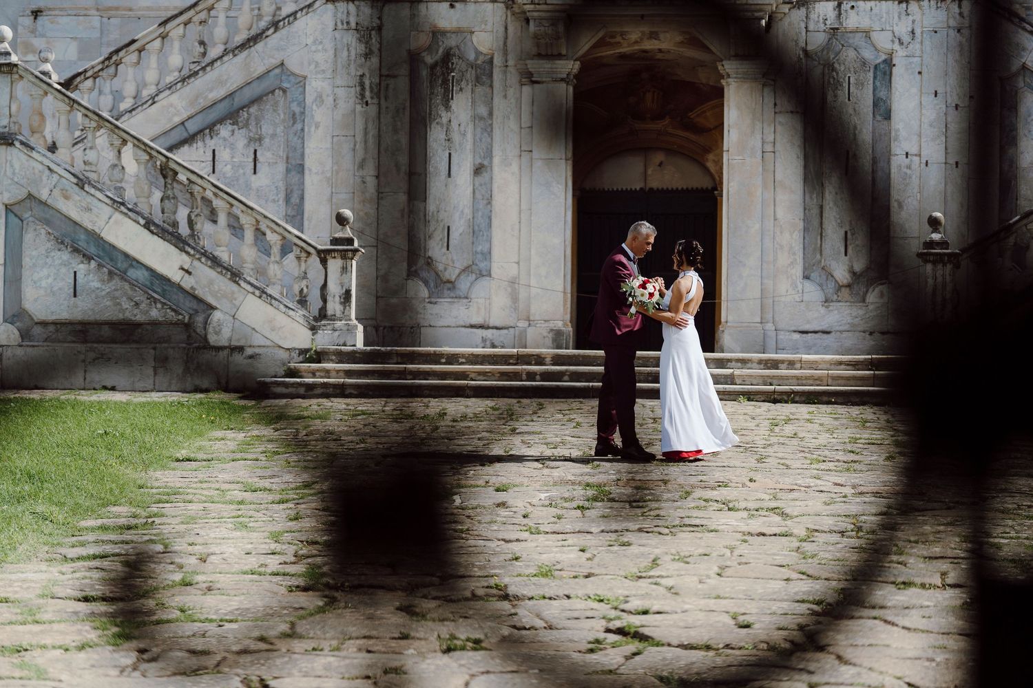 A couple in wedding attire standing on stone steps of a historic building.