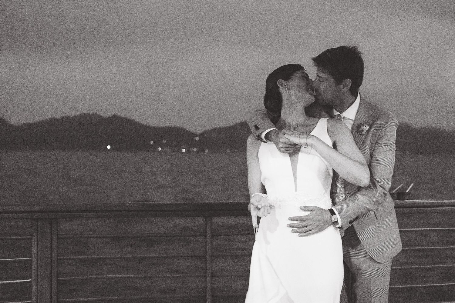 A romantic seaside moment captured in black and white with mountains in the background.