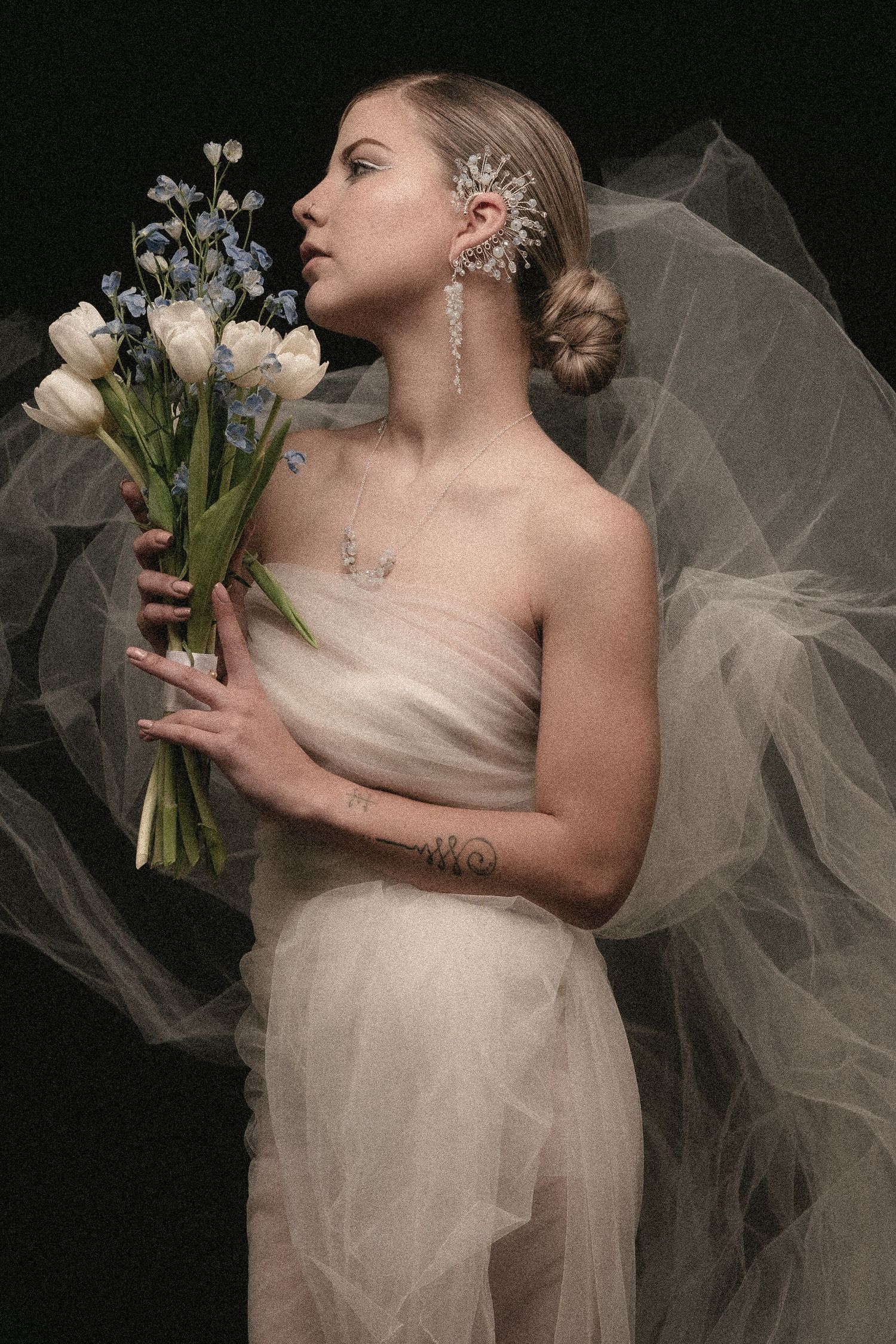 Elegant bridal portrait with white tulips and delicate tulle veil against dark background.