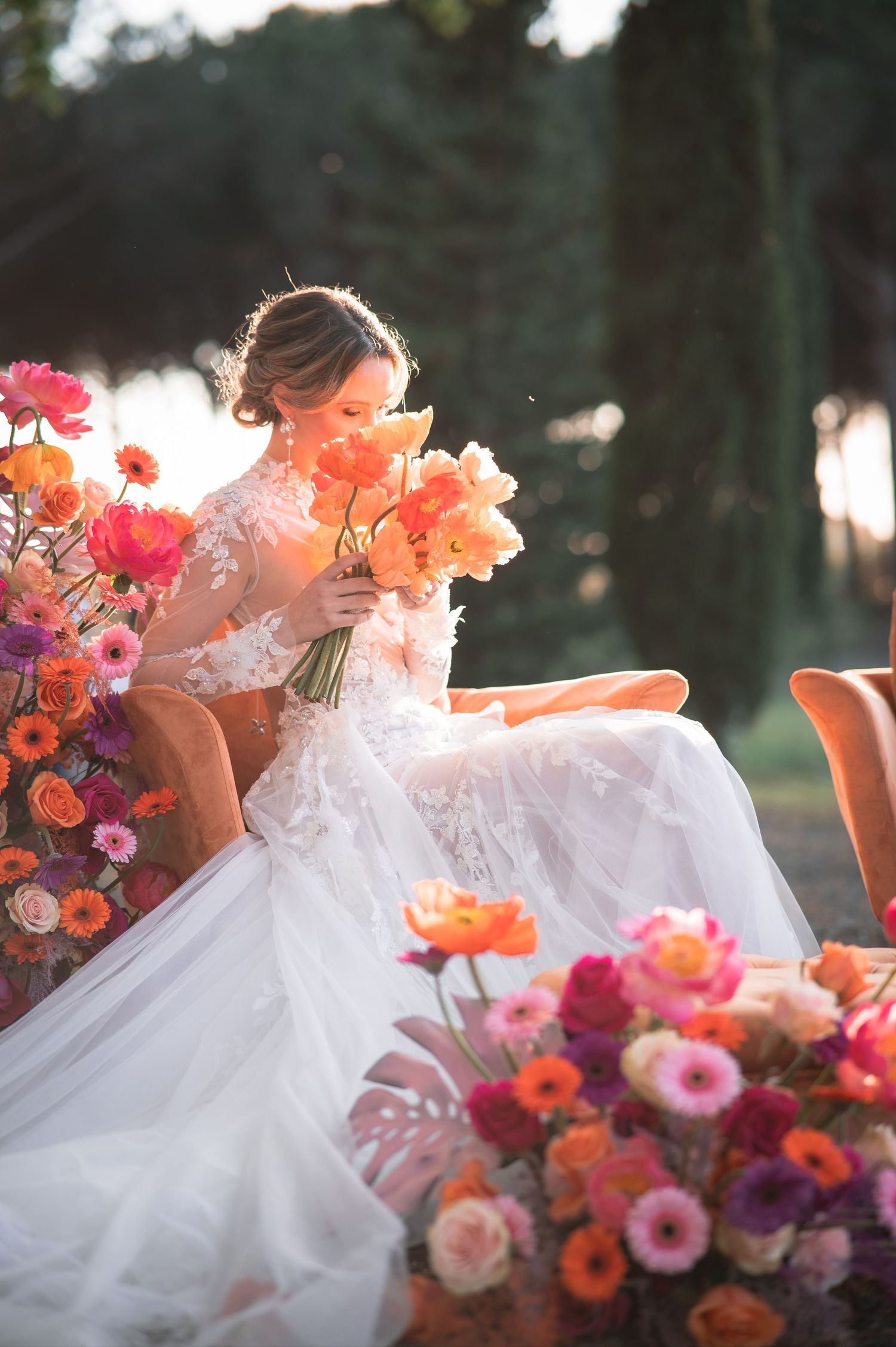 Sunset garden portrait with bride surrounded by coral and pink flower arrangements.