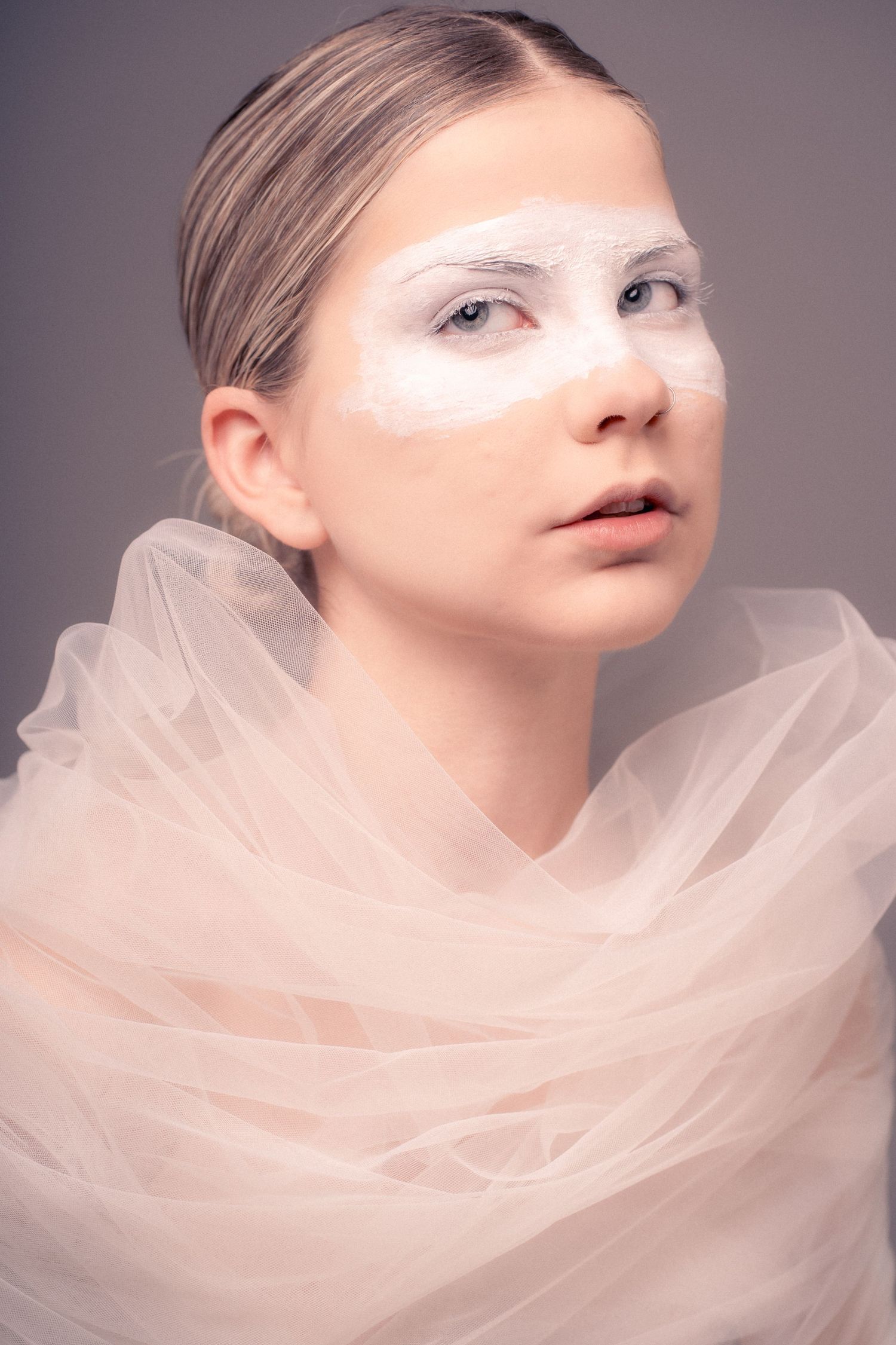 Artistic fashion portrait with delicate white tulle fabric draped around model's neck against neutral grey background.