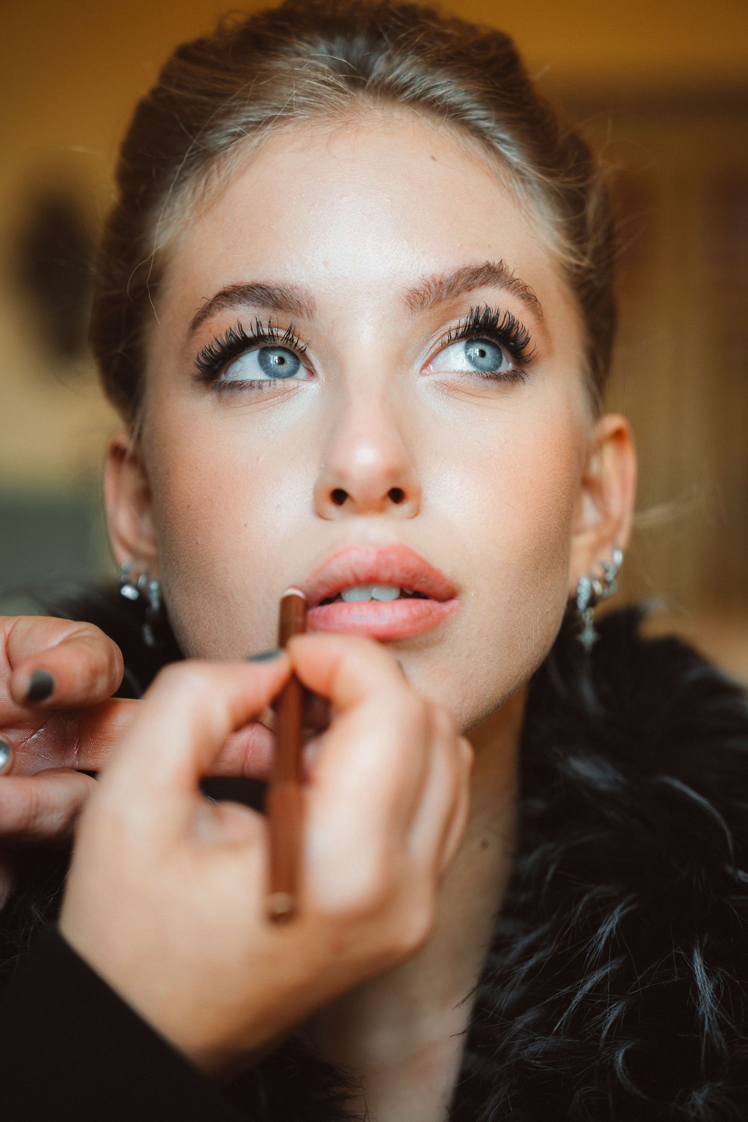 Beauty portrait during makeup application showing bright blue eyes and glossy lips.