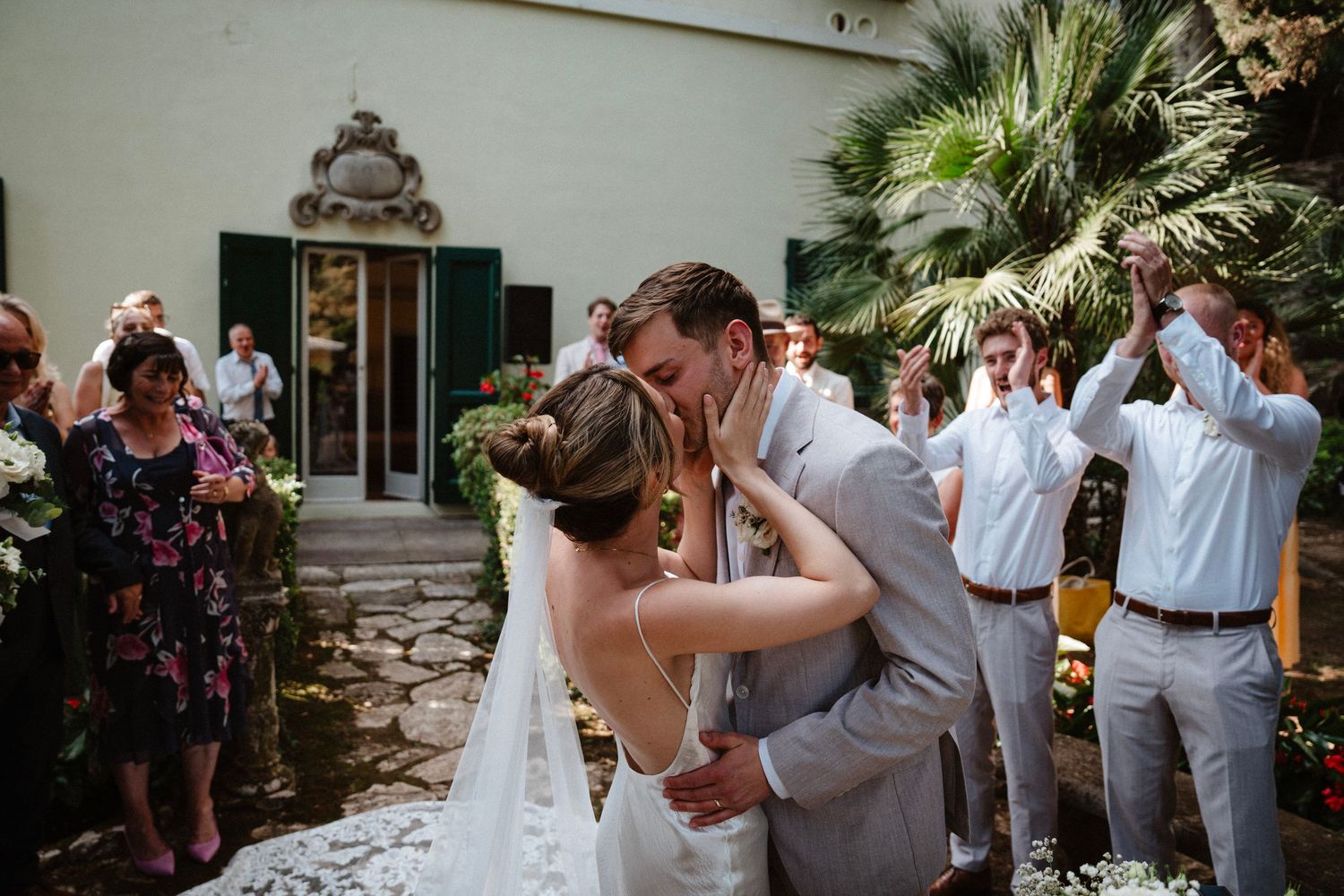 Wedding celebration scene in a garden setting with palm trees and white decor.