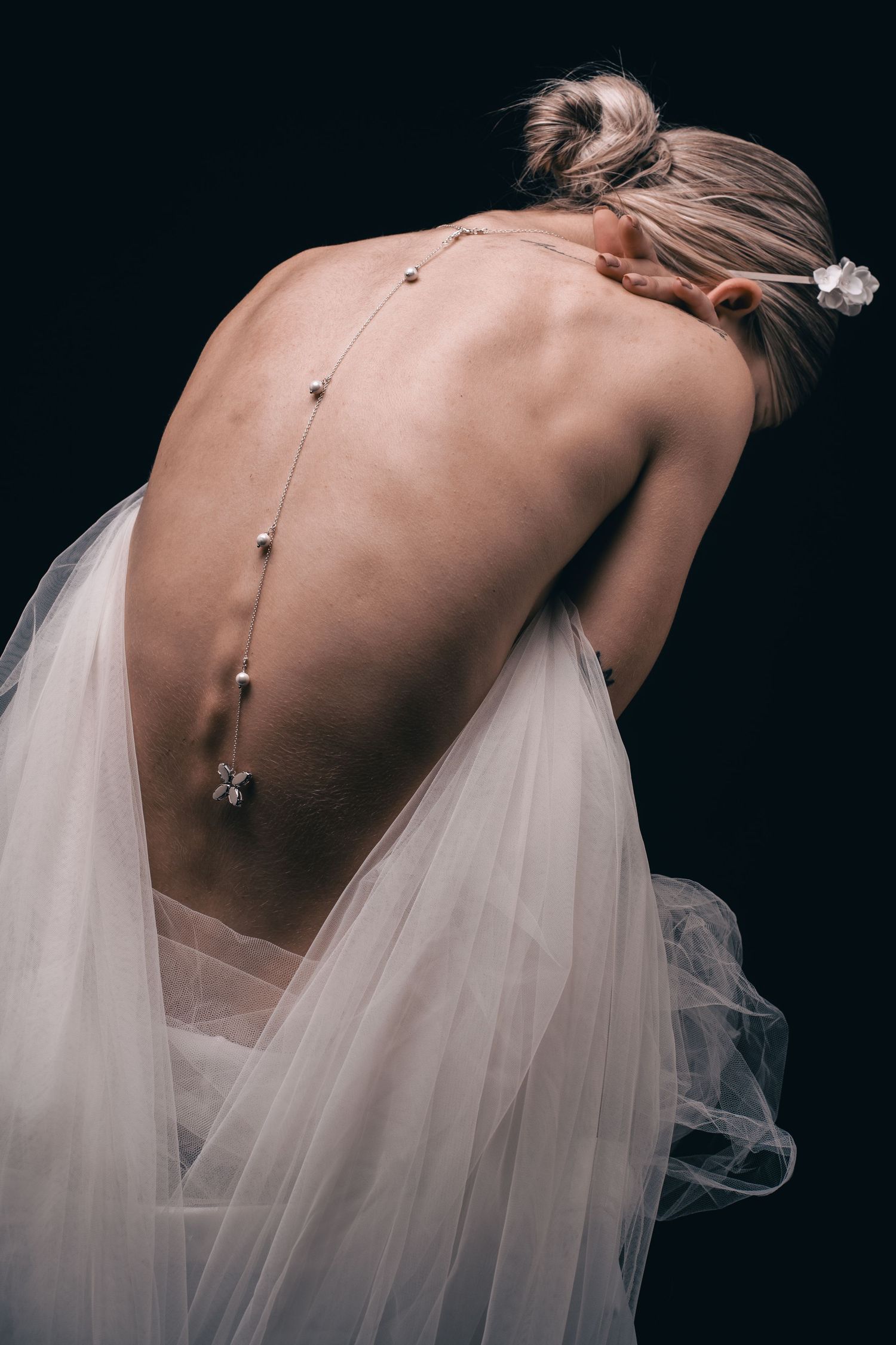 Contemporary bridal photograph showing pearl details on bare back with flowing veil.
