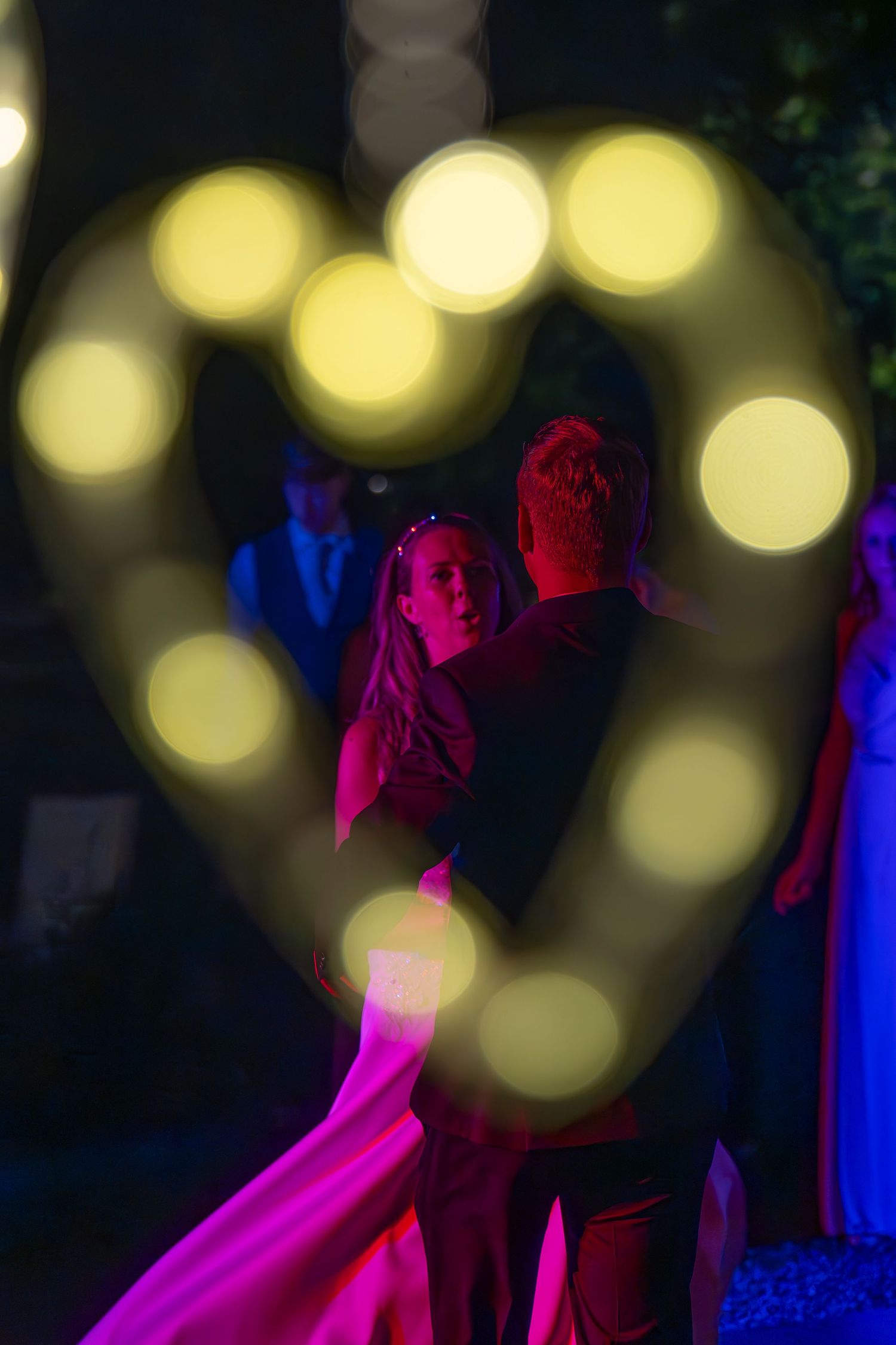 A creative night photo with bokeh lights forming a heart shape at a wedding reception.