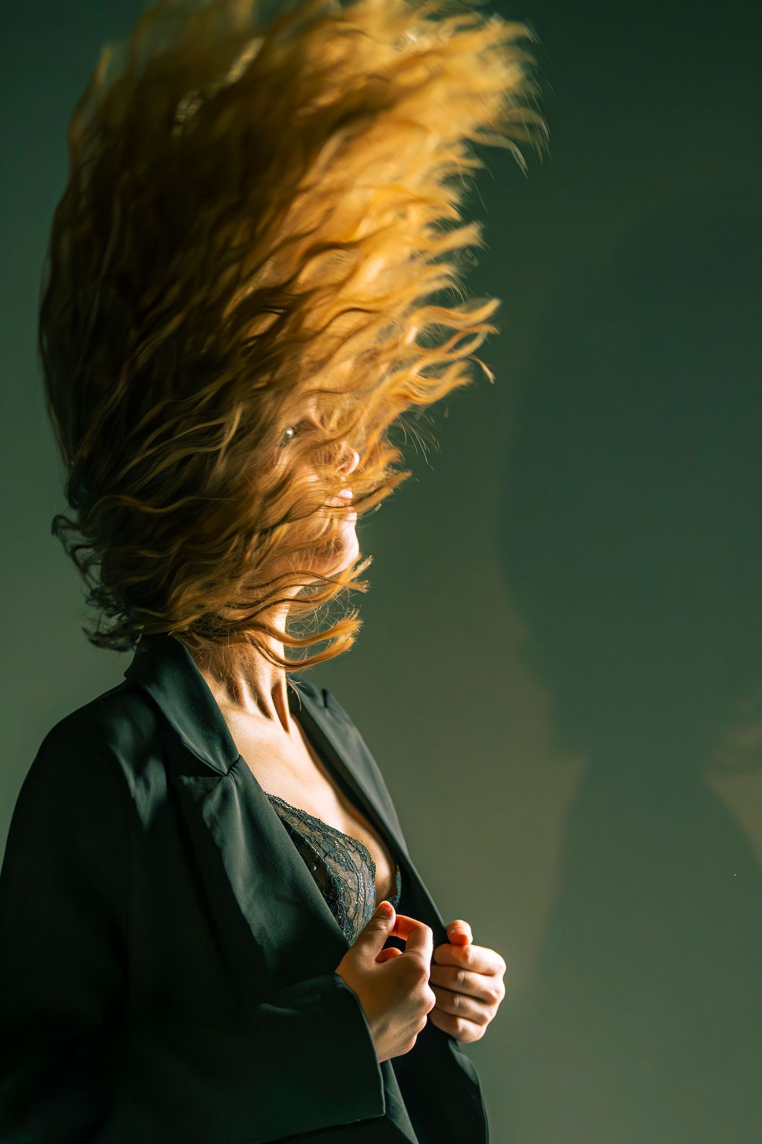 Artistic portrait of flowing blonde hair movement against dark green background.