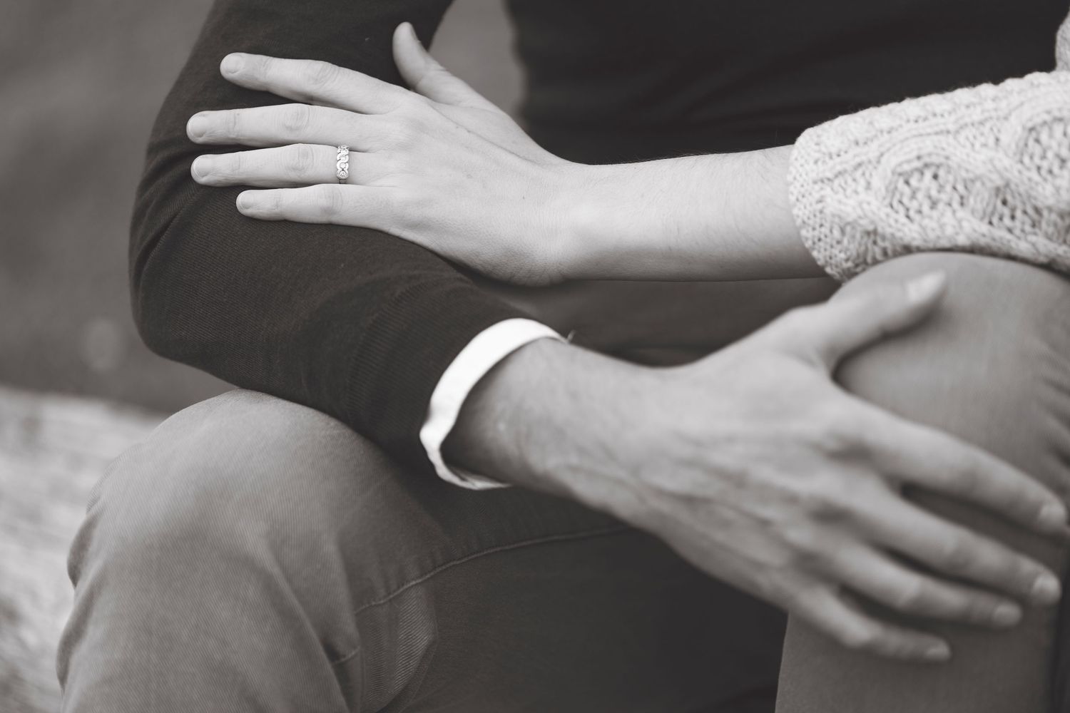 Close-up black and white photo showing hands embracing during romantic couple moment.