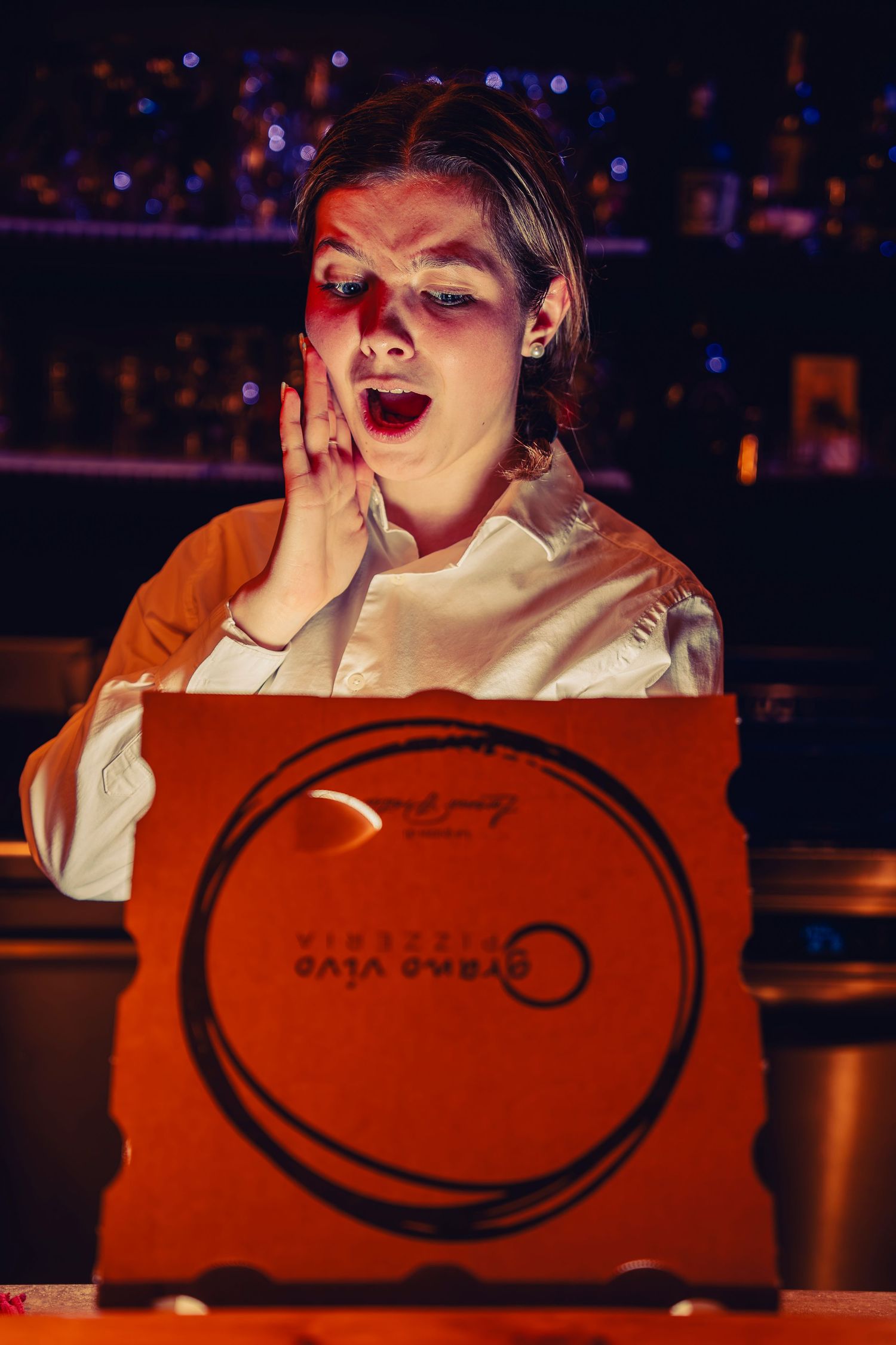 Night scene at bar with person reacting excitedly to glowing red takeout box.