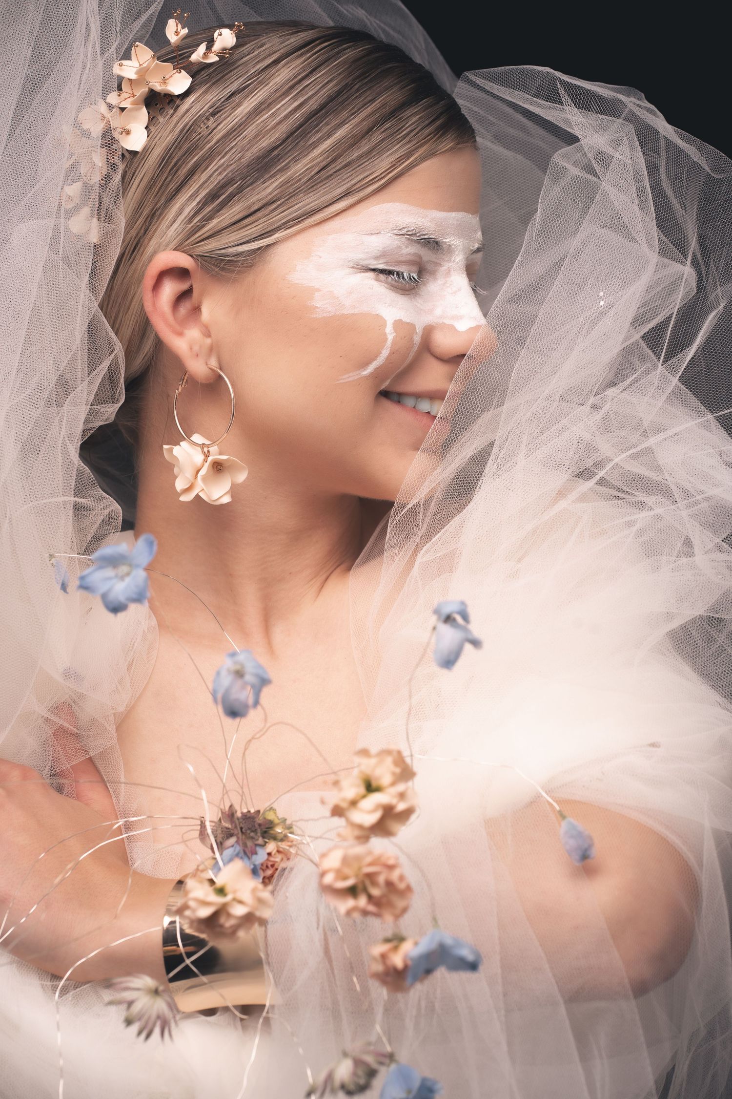 Ethereal beauty shot with tulle fabric and scattered dried flowers in peach and blue tones.