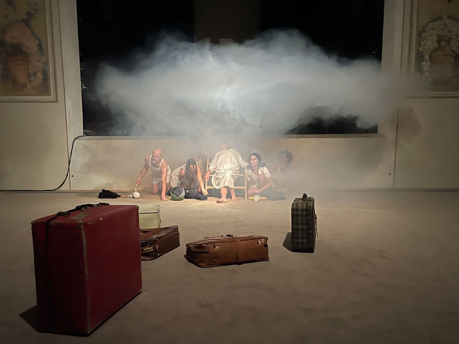 Atmospheric stage setup with smoke and vintage suitcases illuminated by warm lights.