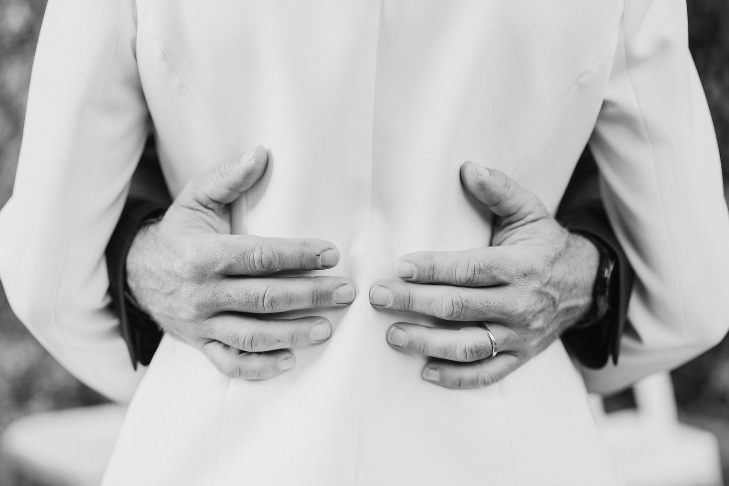 A close-up black and white photo of hands tenderly placed on a white dress.