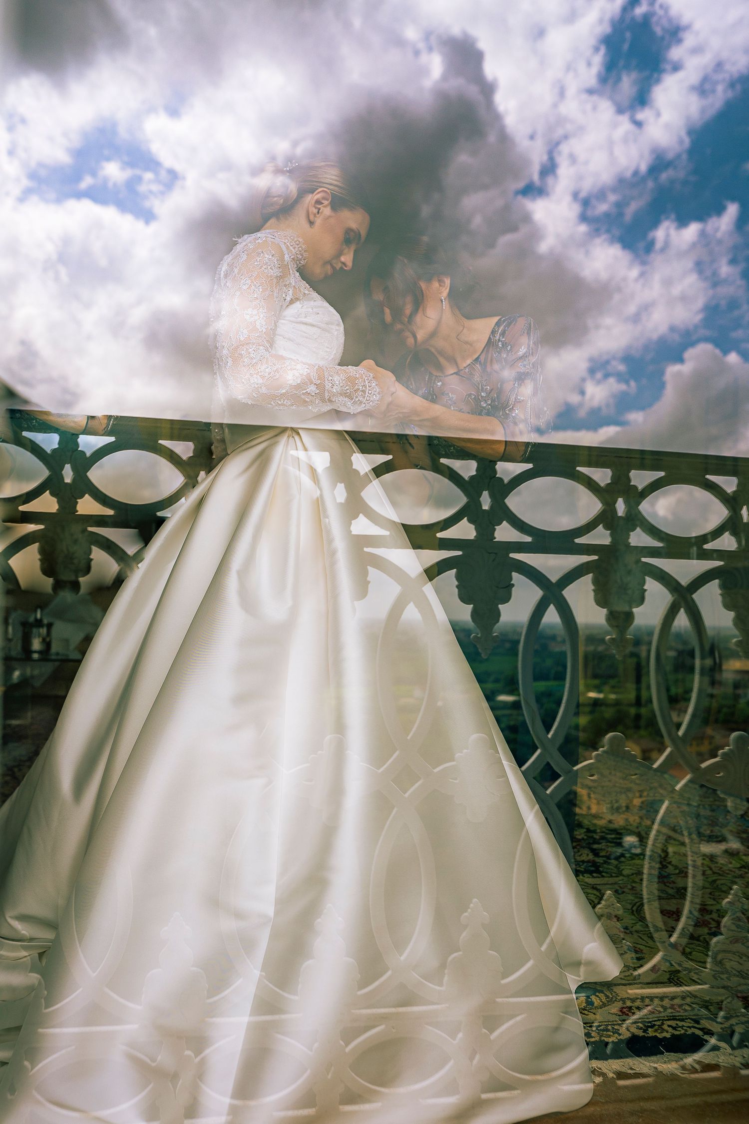 A dreamy wedding photo of a couple on an ornate balcony against cloudy skies.
