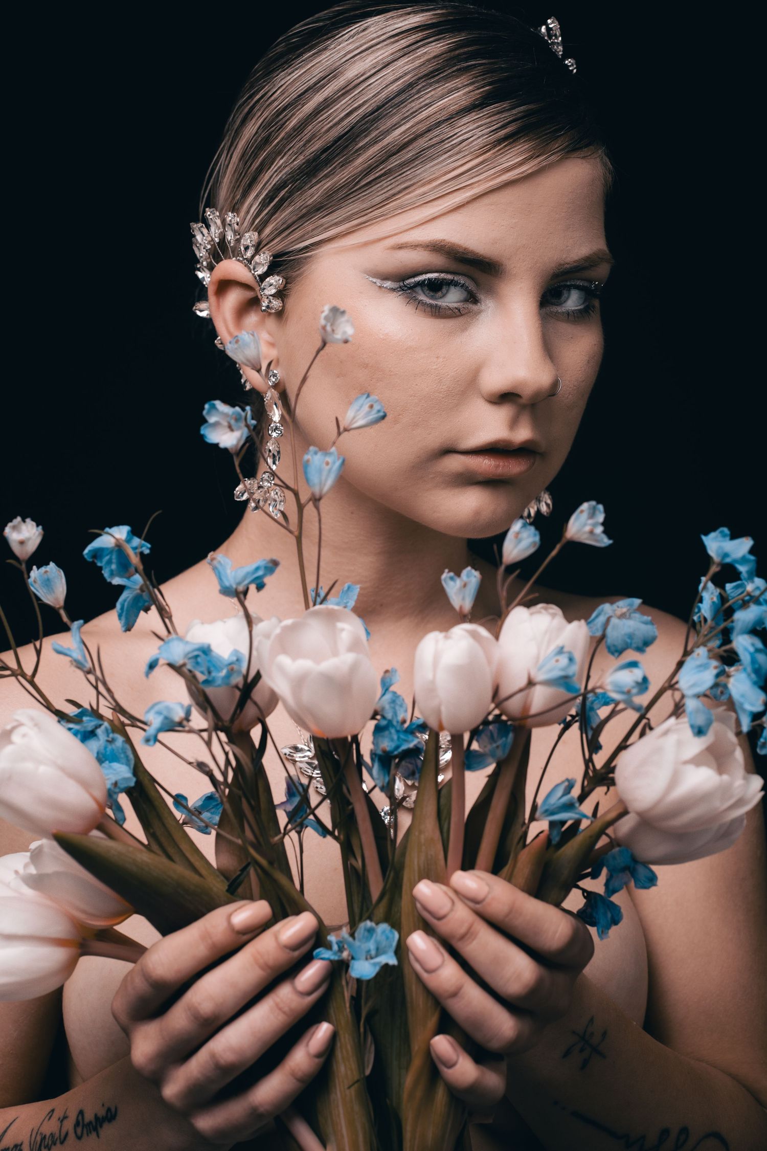 Ethereal bridal portrait with delicate blue and white flowers against dark background.