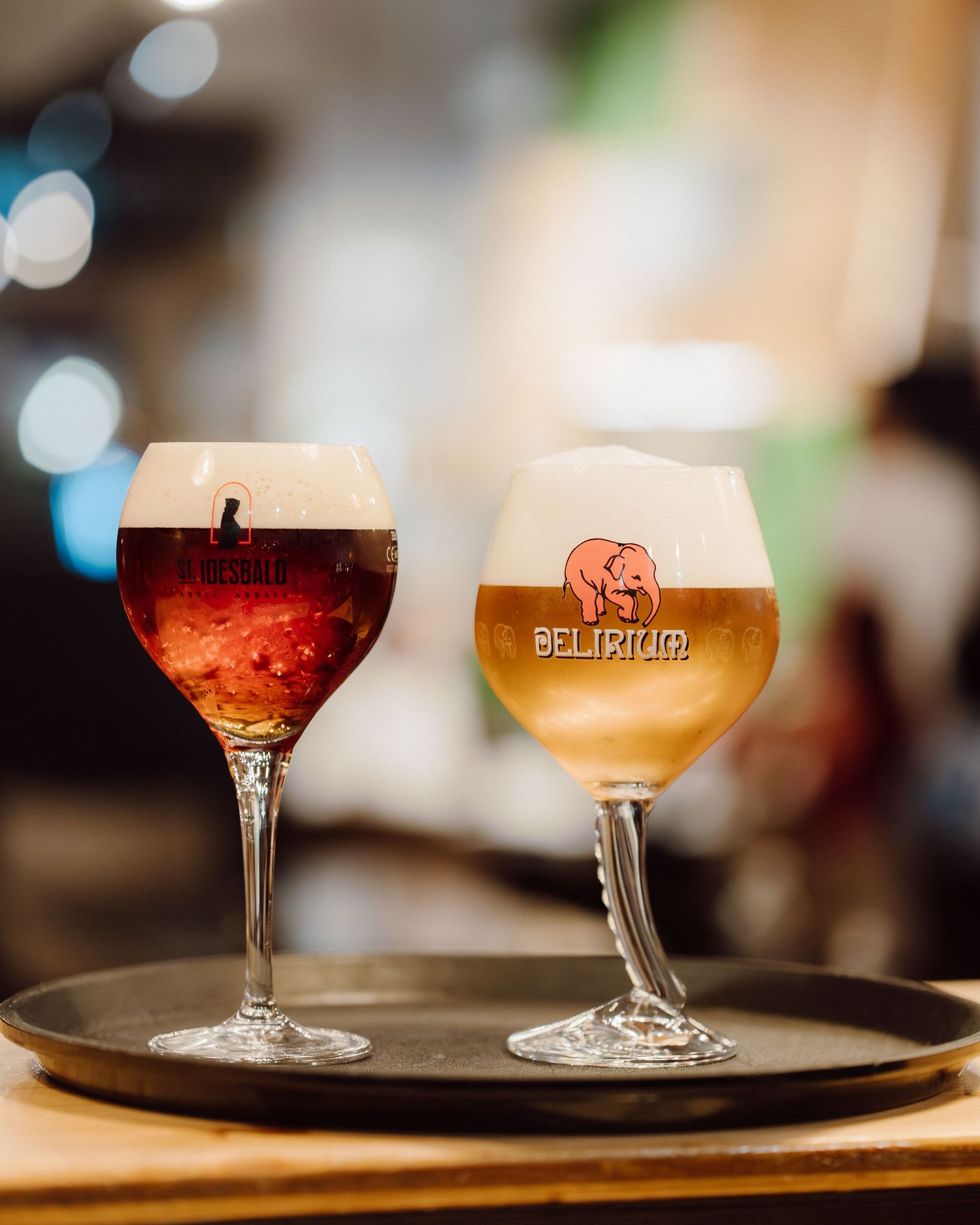 Two different craft beers served in stemmed glasses on a wooden serving tray.