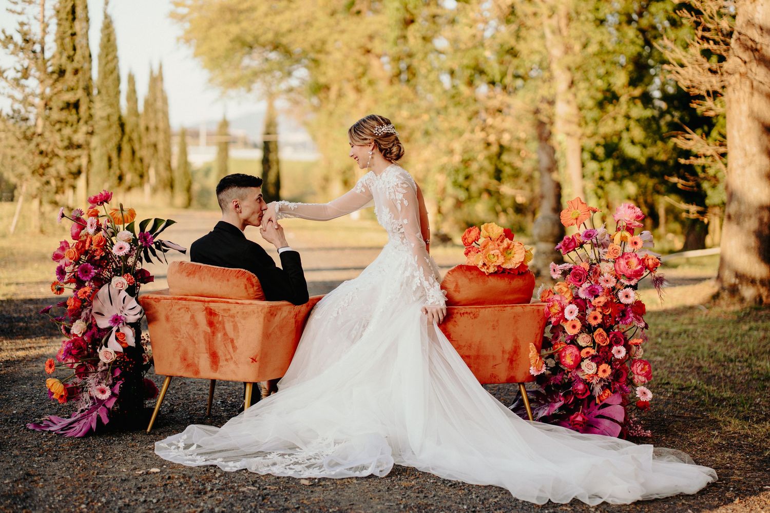 A unique wedding moment with the couple sitting on a vintage floral sofa, surrounded by nature and decorative flowers.