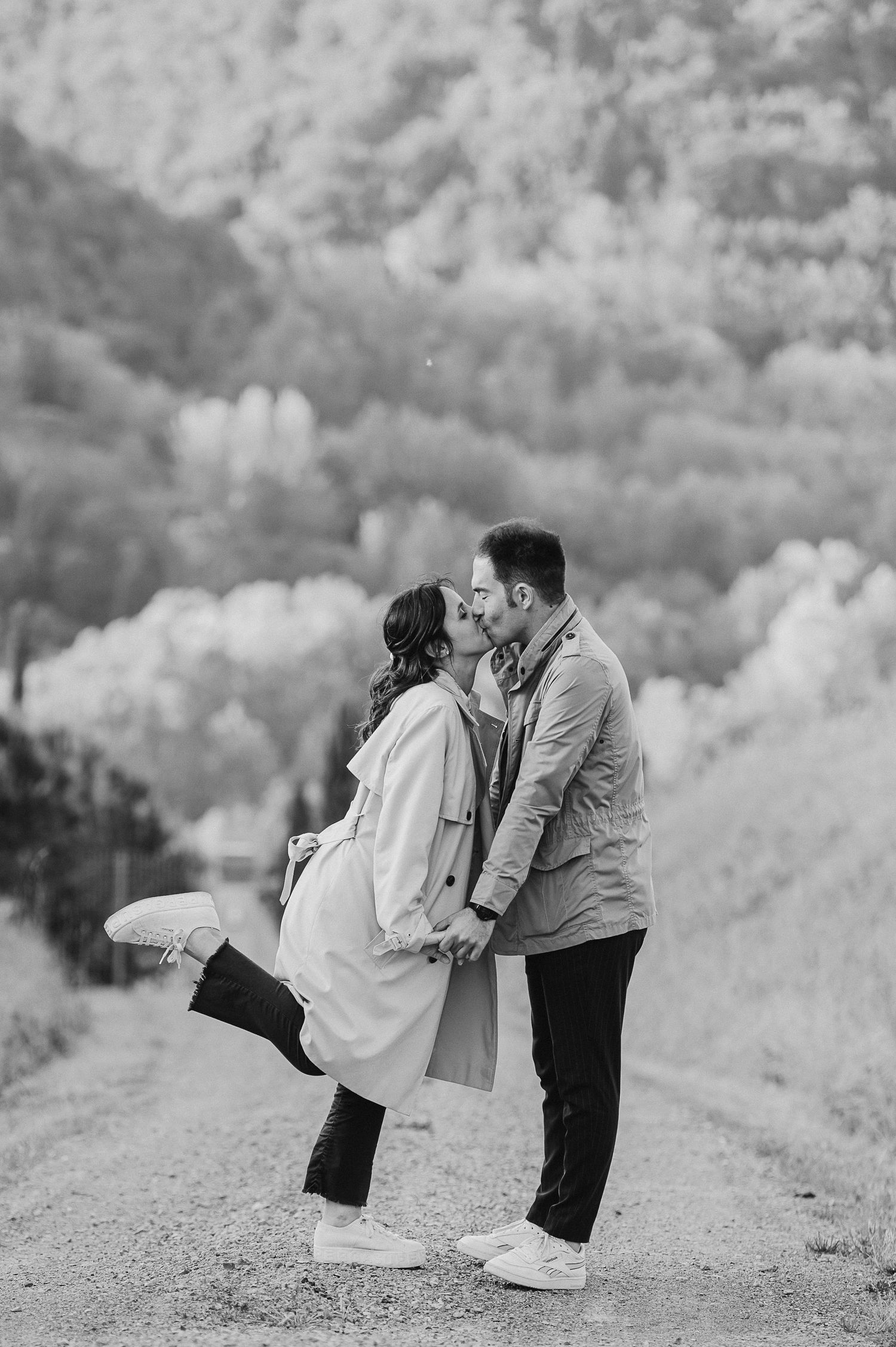 A black and white photo of a couple sharing a romantic moment on a mountain path.