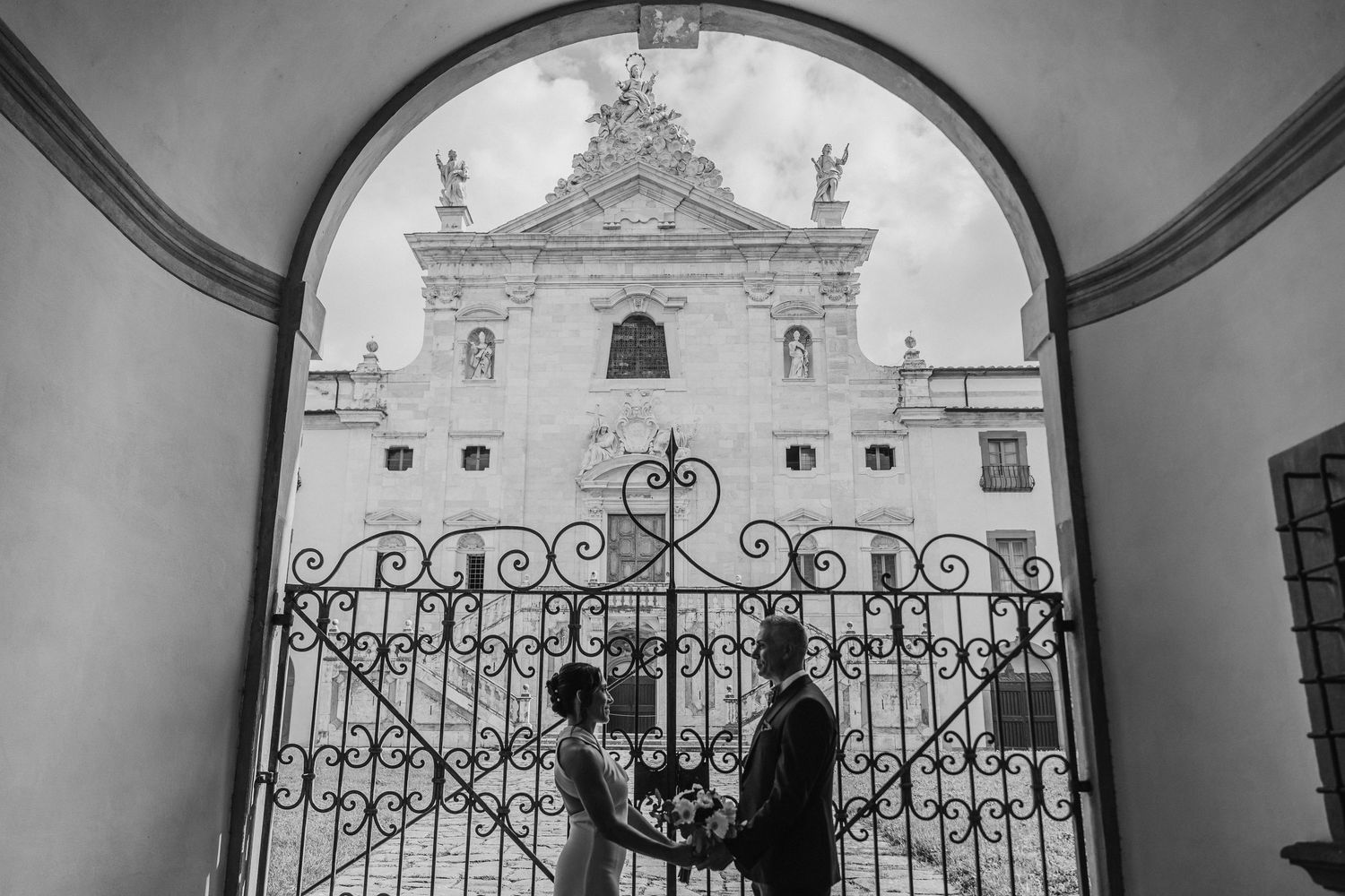 A romantic silhouette of a couple through an ornate archway entrance to a historic building.