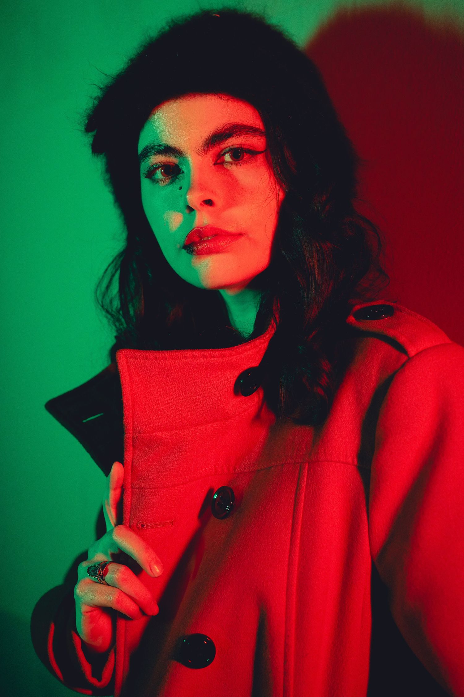 Portrait with dramatic red and green lighting wearing a bright red winter coat.