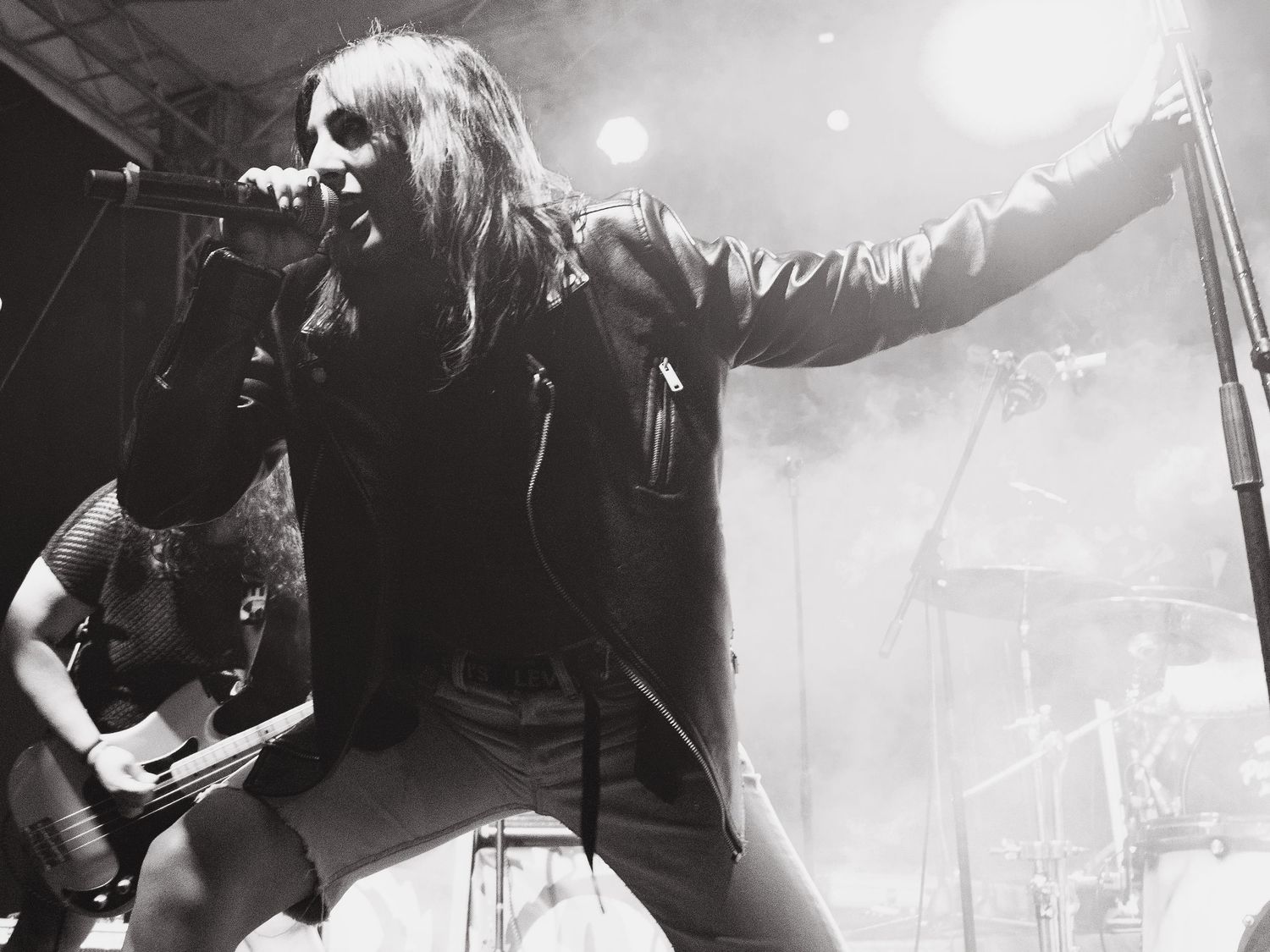 Black and white concert photo of performer singing on stage with guitarist in background.