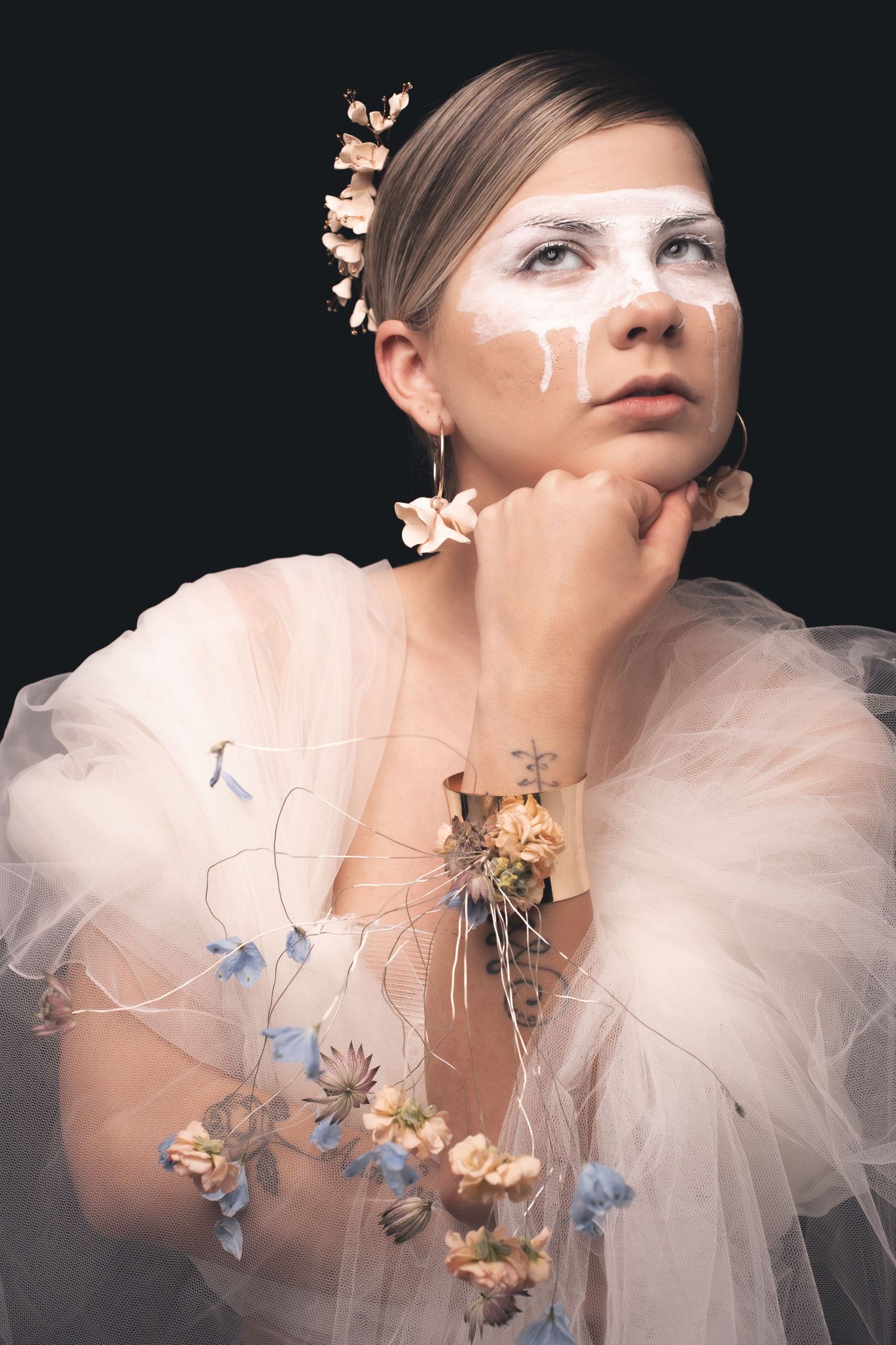 Artistic photo with white face paint and floral accessories against dark backdrop.