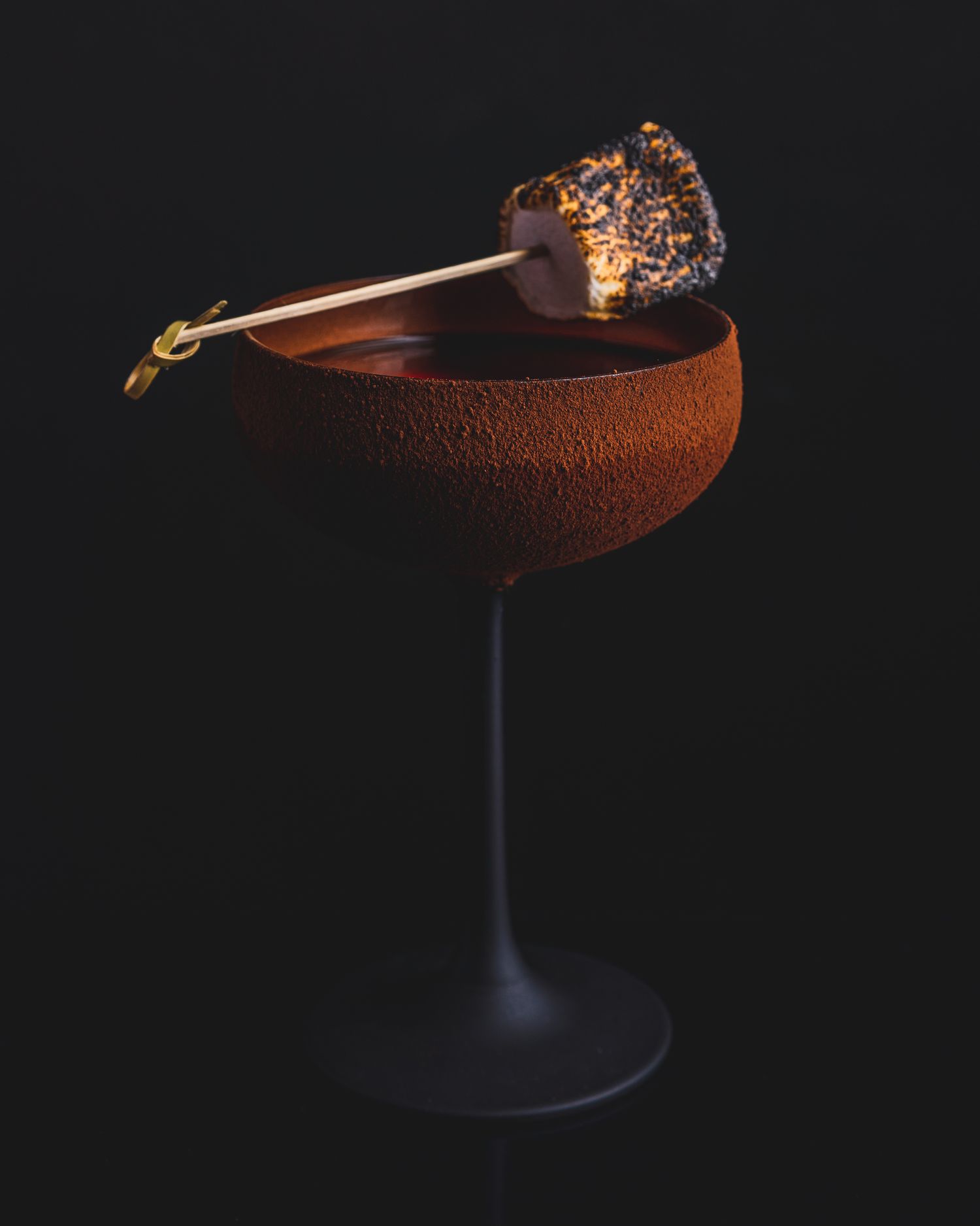 Elegant chocolate cocktail with garnish in a coupe glass against dark background.