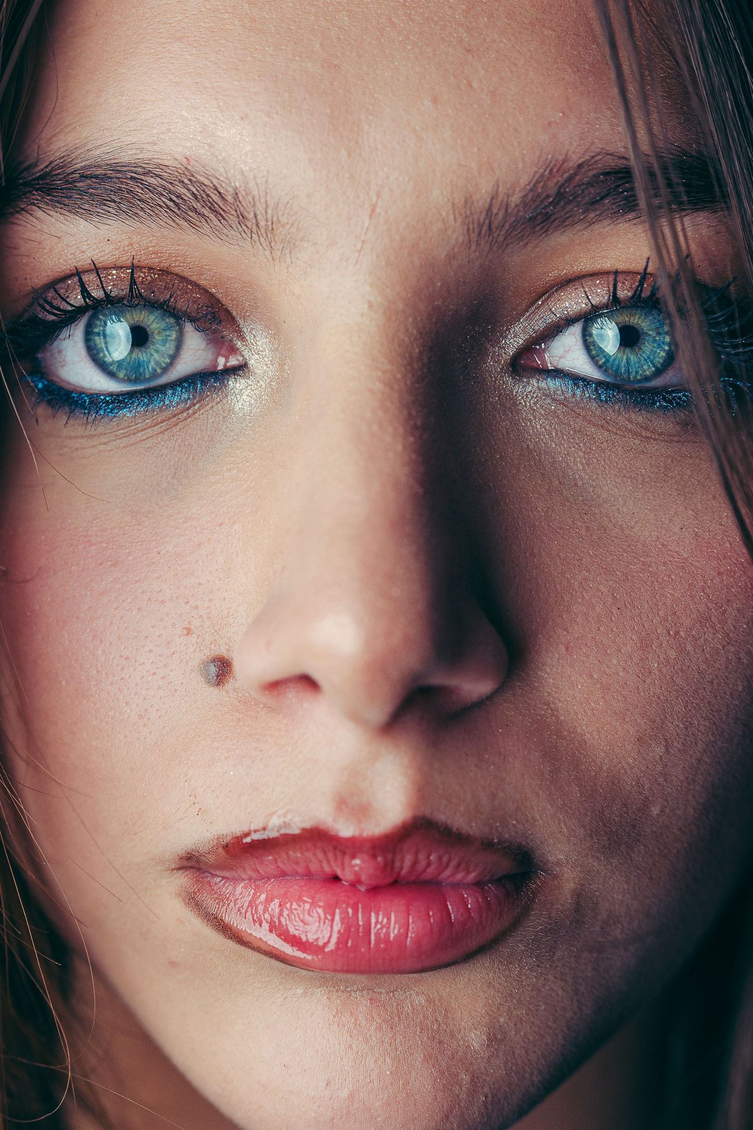 Extreme closeup portrait showing striking blue eyes, pink lips, and a beauty mark.