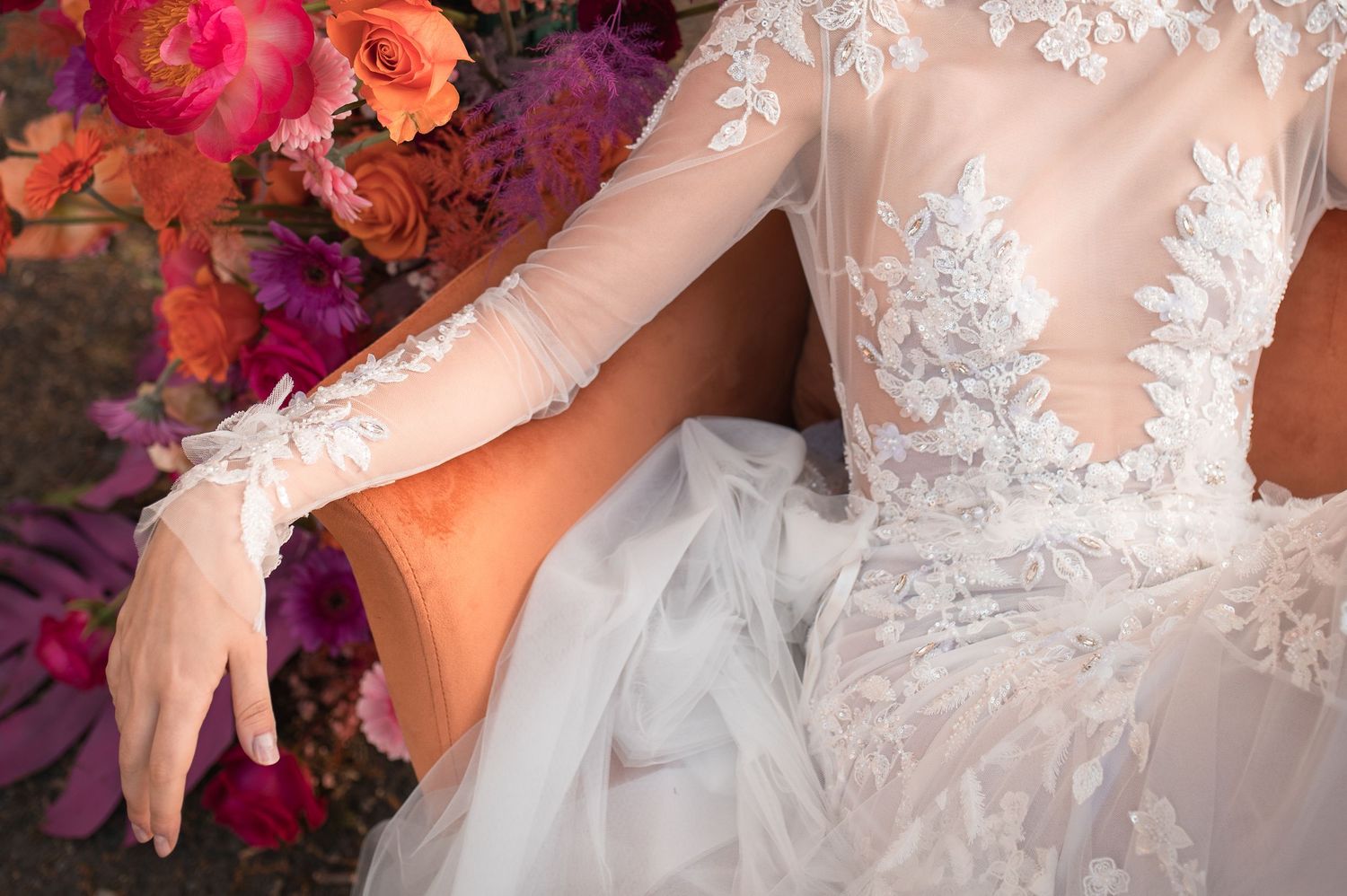 Detail shot of lace wedding dress sleeve with pink and orange floral arrangements.