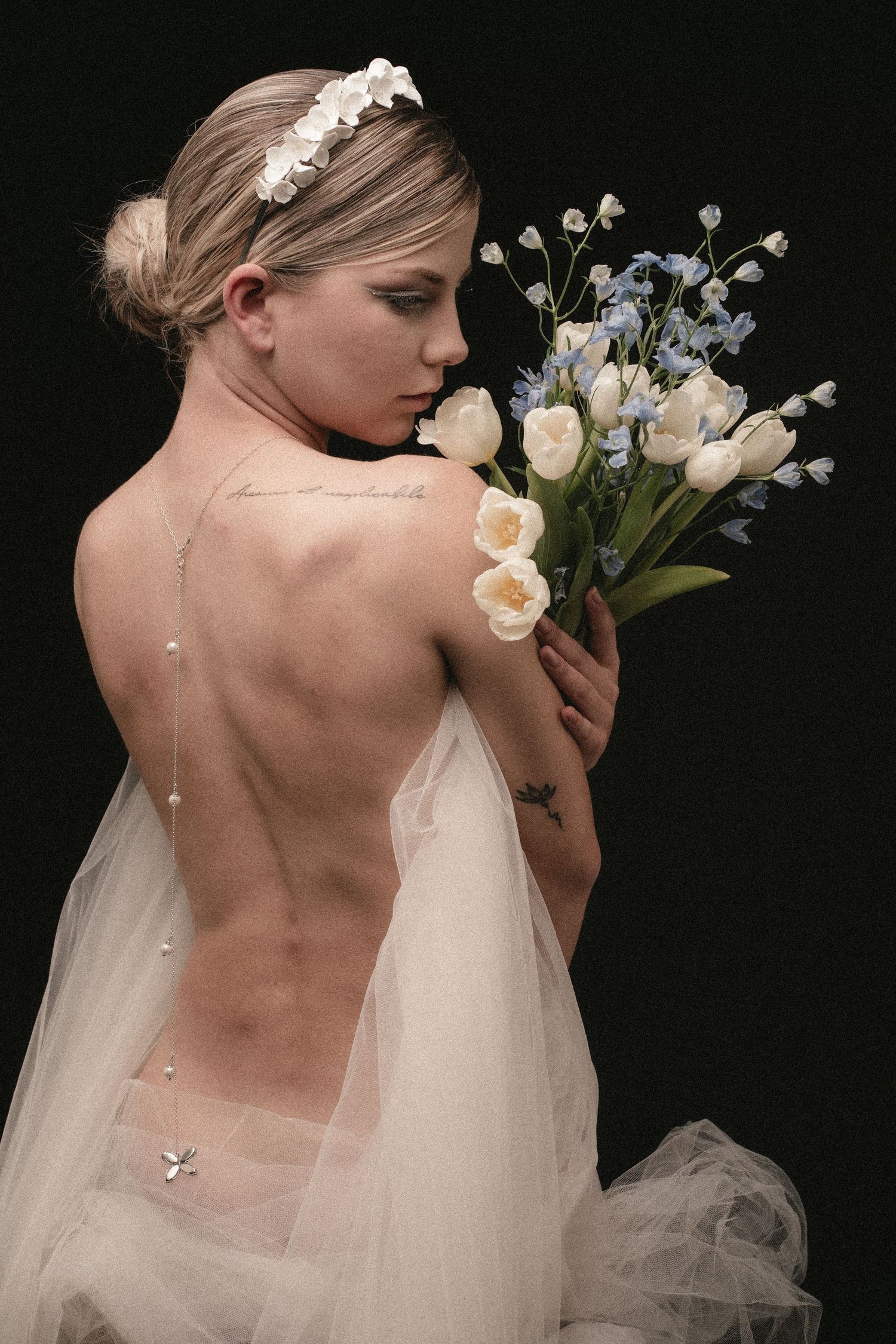 Dramatic bridal portrait with flowing veil and bouquet against black background.